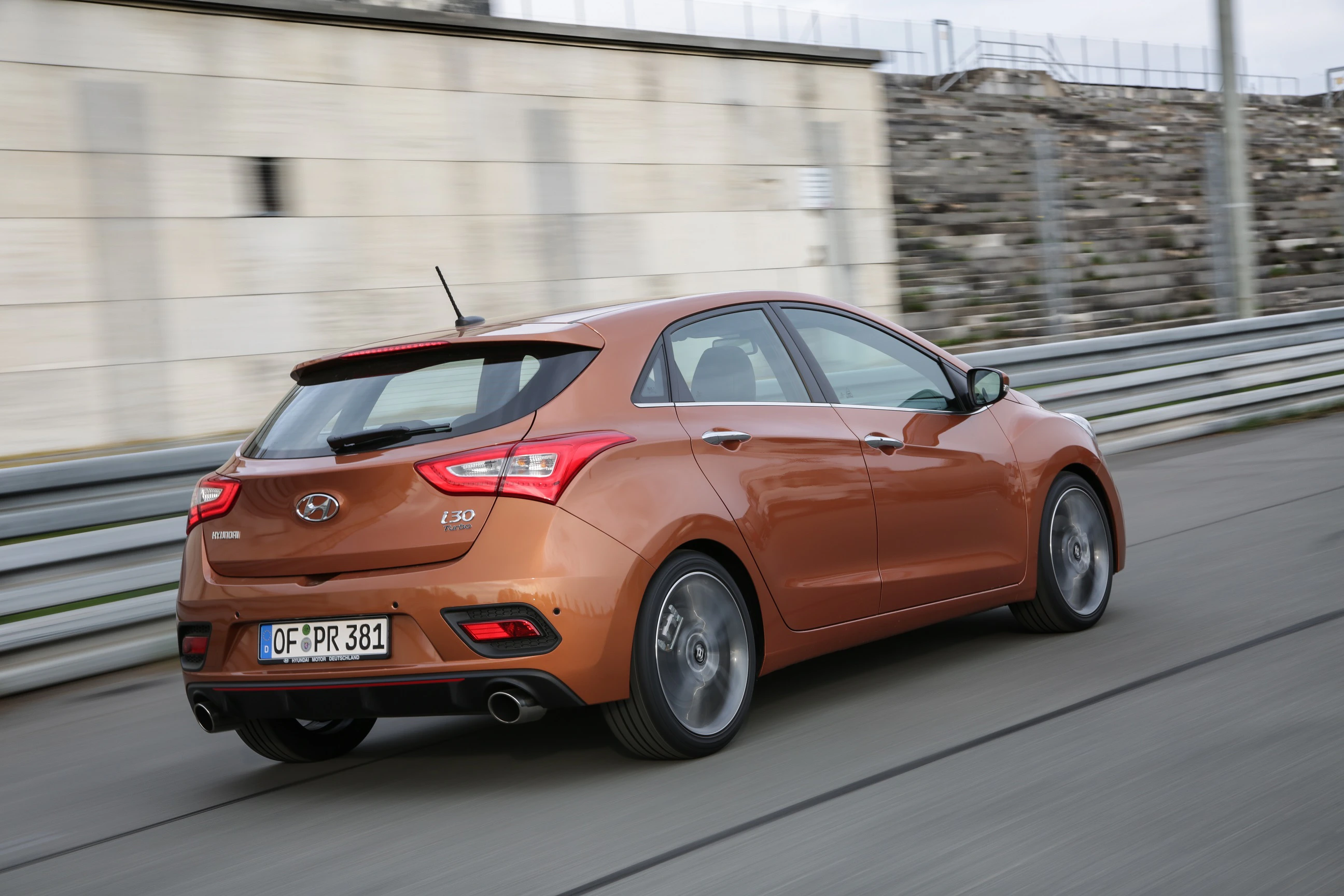 Ein brauner Hyundai i30 fährt mit hoher Geschwindigkeit auf einer Rennstrecke, Mauern und Begrenzungen im Hintergrund.