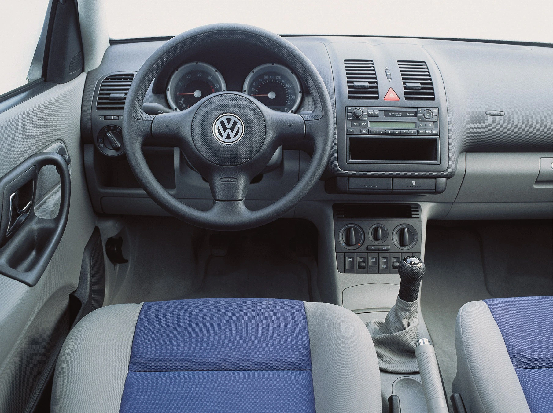 Innenraum eines Autos mit Volkswagen-Logo auf dem Lenkrad. Sichtbar sind das Armaturenbrett, Schaltknüppel und blaue Sitzbezüge.