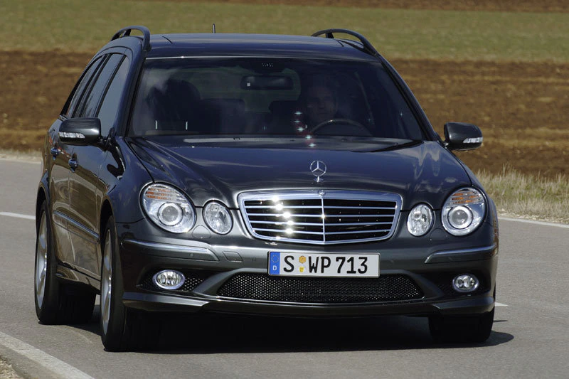 Schwarzer Mercedes Kombi fährt auf einer Landstraße. Fahrzeugfront mit markantem Kühlergrill und Scheinwerfern im Fokus.