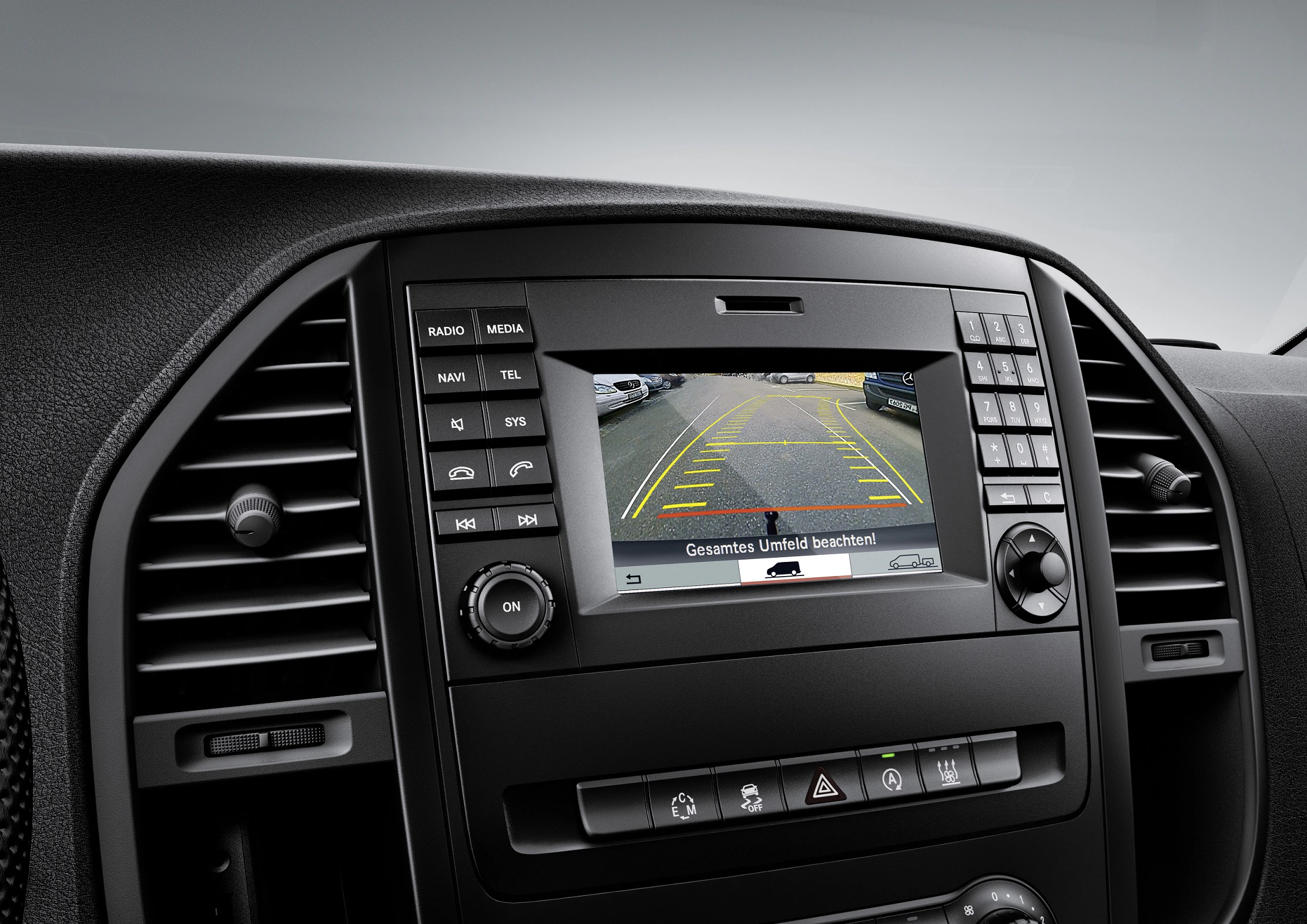 Autoinnenraum mit Rückfahrkameraanzeige auf Bildschirm. Tasten für Radio, Navi und Telefon sind neben dem Display sichtbar.