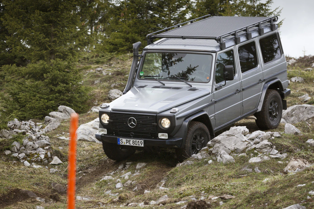 Geländewagen fährt über steiniges, unebenes Gelände im Wald. Der Himmel ist leicht bewölkt.