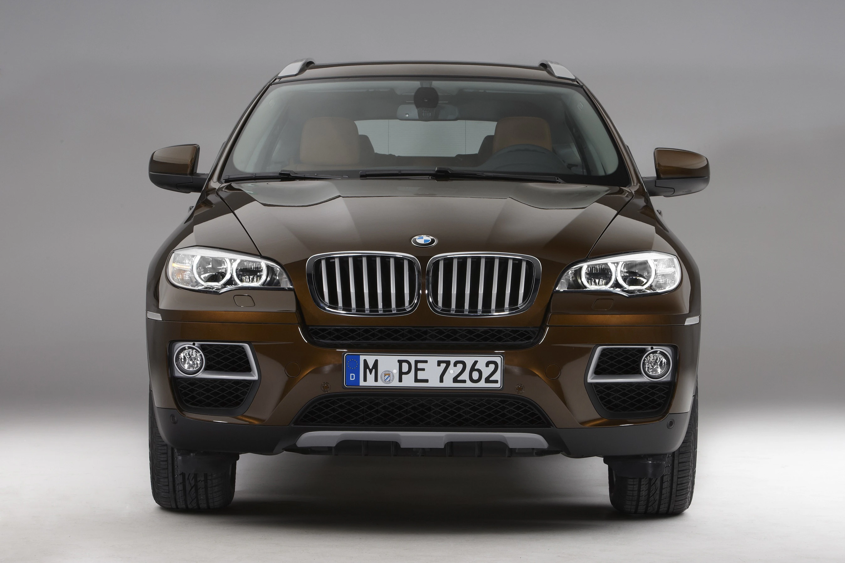 Brauner BMW-SUV von vorne, grauer Hintergrund, kennzeichen "M PE 7262", moderne Scheinwerfer und markantes Design.
