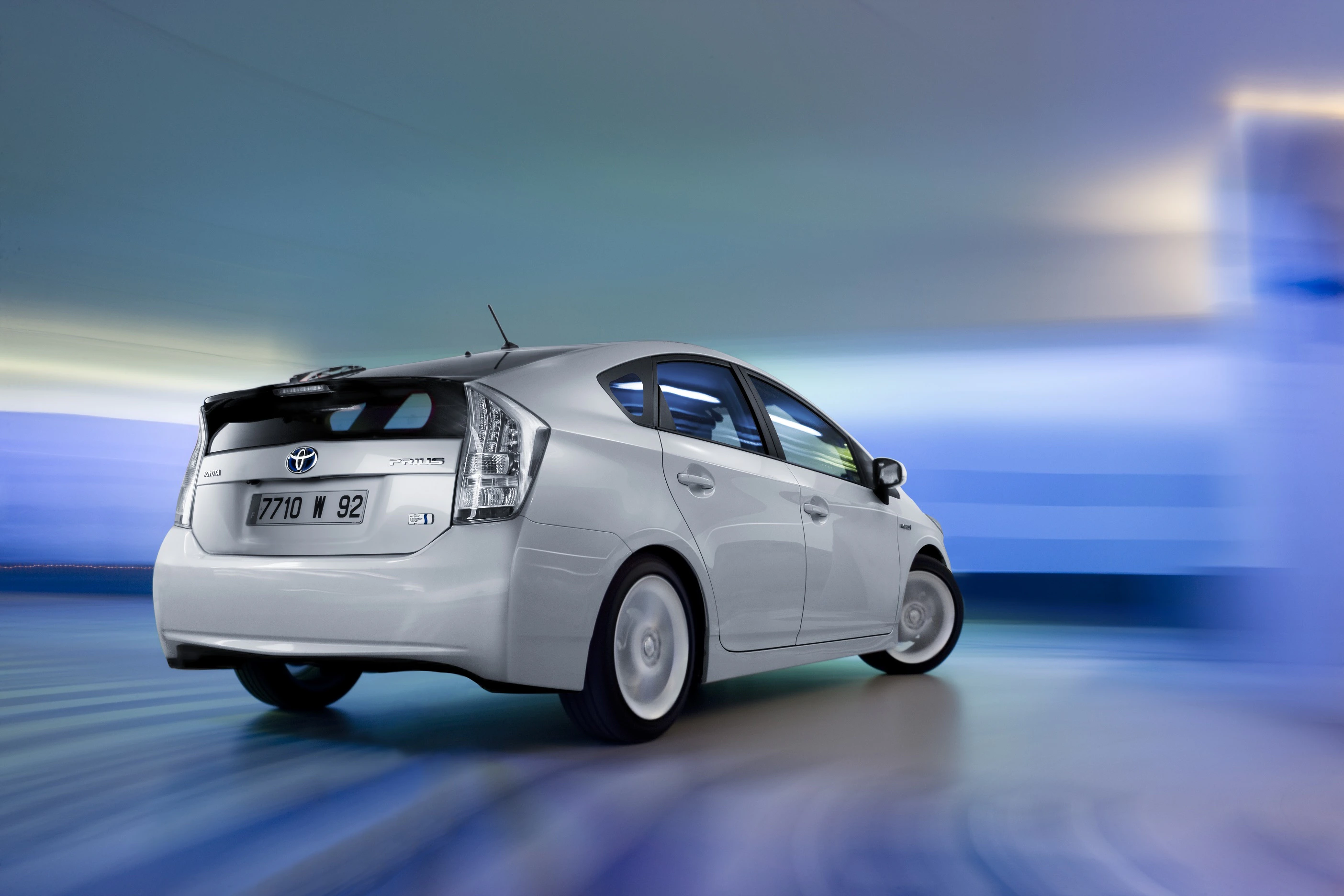 Silberner Toyota Prius fährt in einem verschwommenen, futuristischen Tunnel mit blauen und grünen Akzenten.