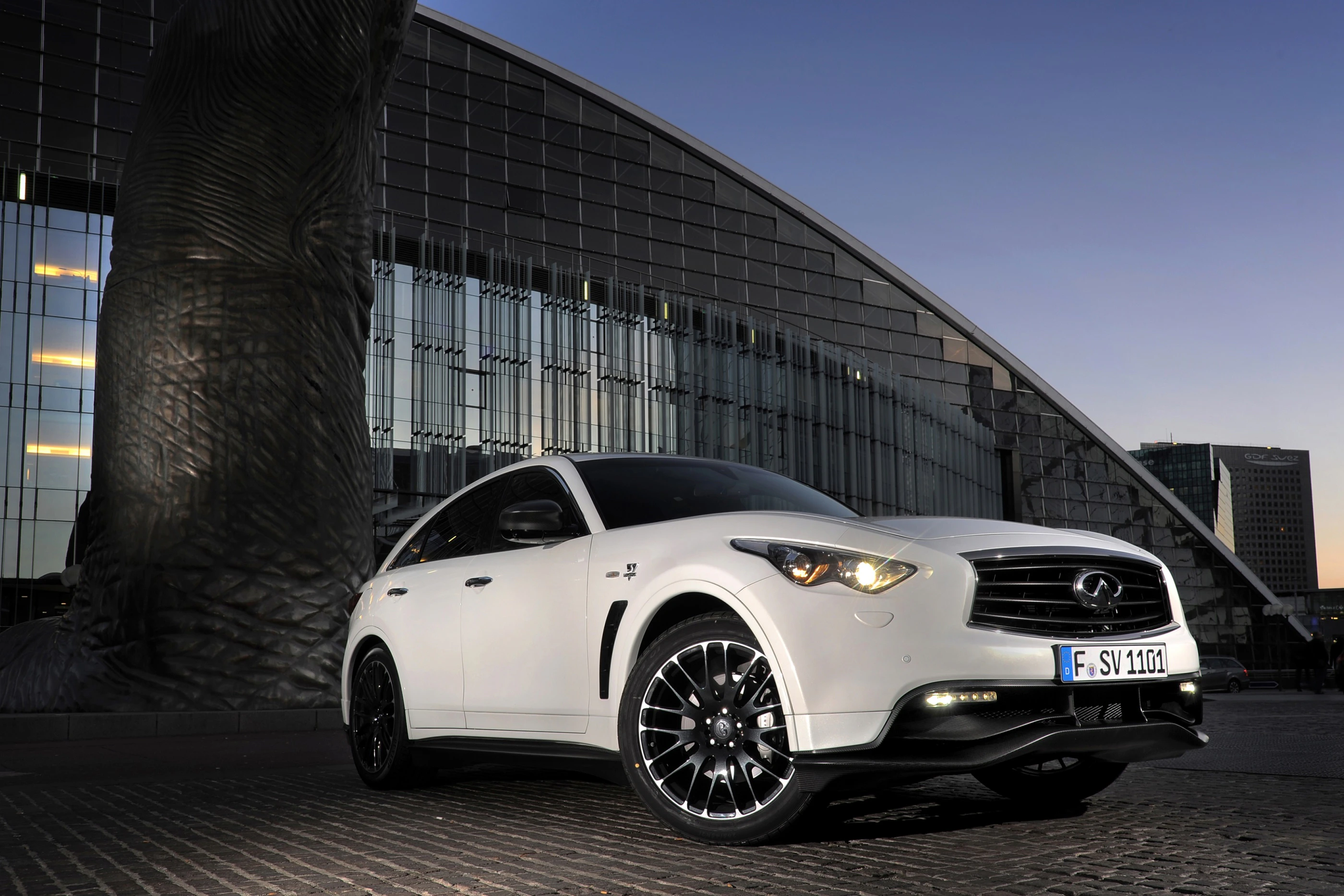 Weißer SUV vor modernem, beleuchtetem Gebäude bei Dämmerung. Elegantes Design mit schwarzen Felgen.