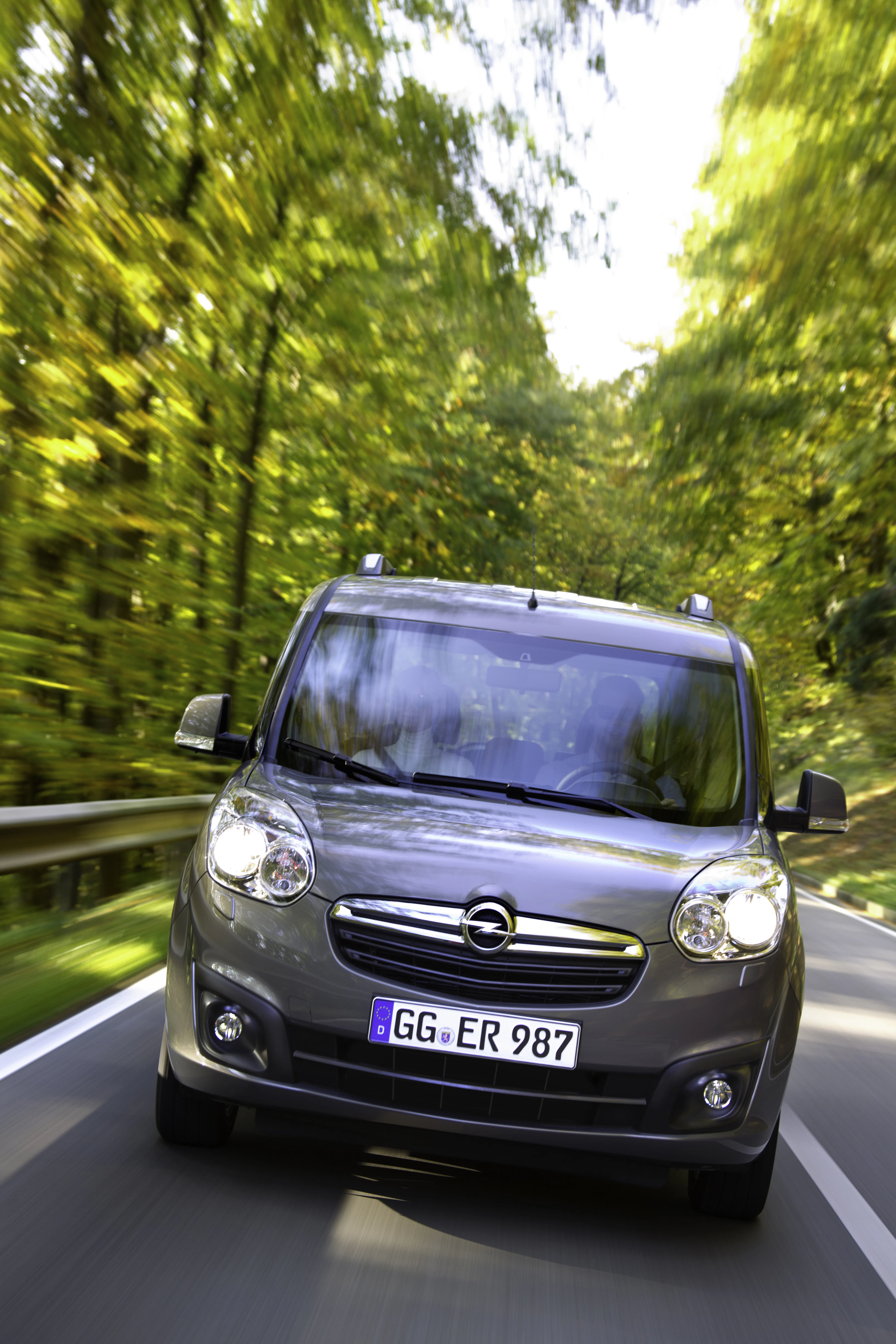 Silberner Opel-Kleintransporter fährt auf einer Straße durch einen Wald bei Tageslicht. Verschwommener Hintergrund deutet auf Geschwindigkeit hin.