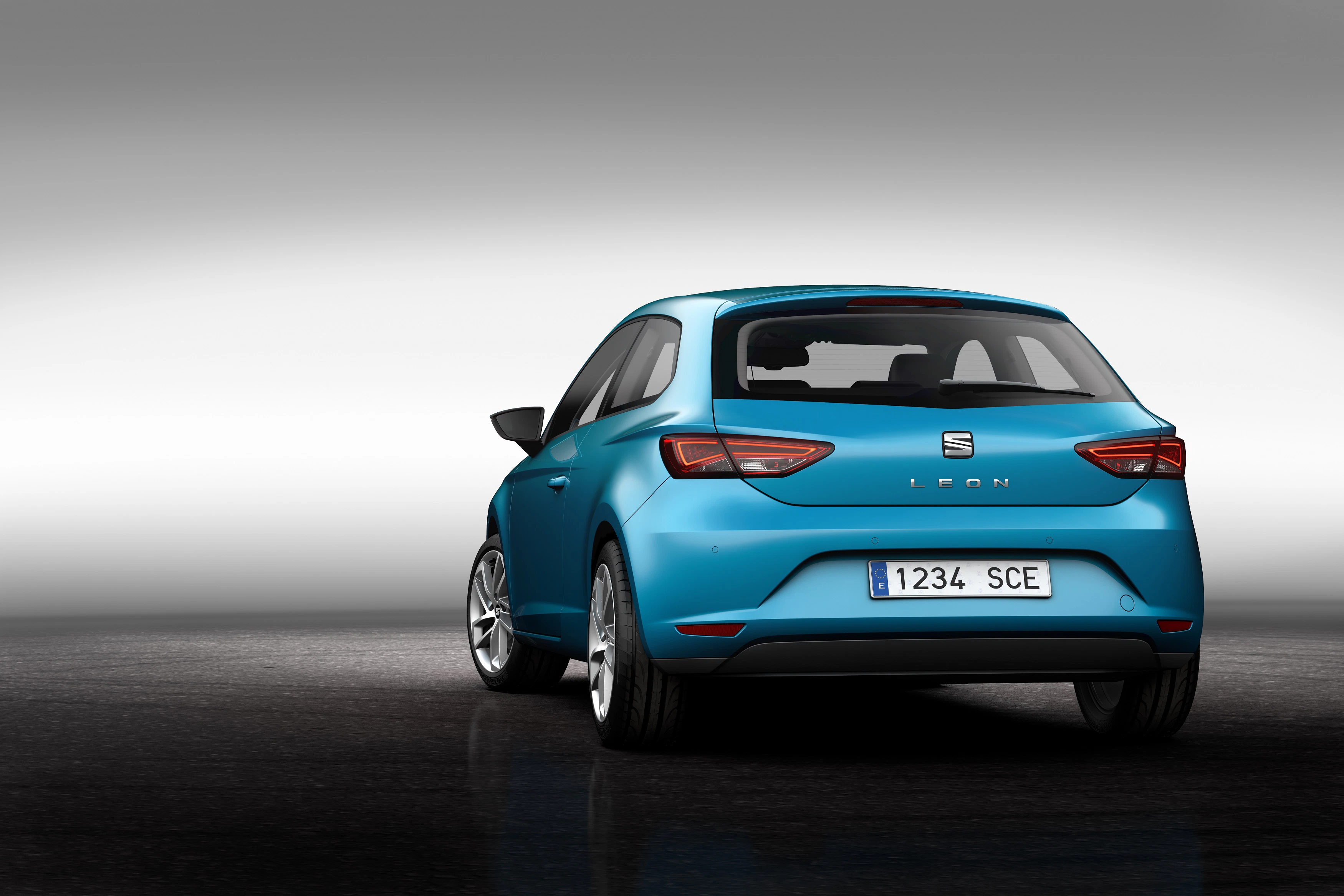Blauer Seat Leon auf dunklem, reflektierendem Boden vor grauem Hintergrund, von hinten gesehen.