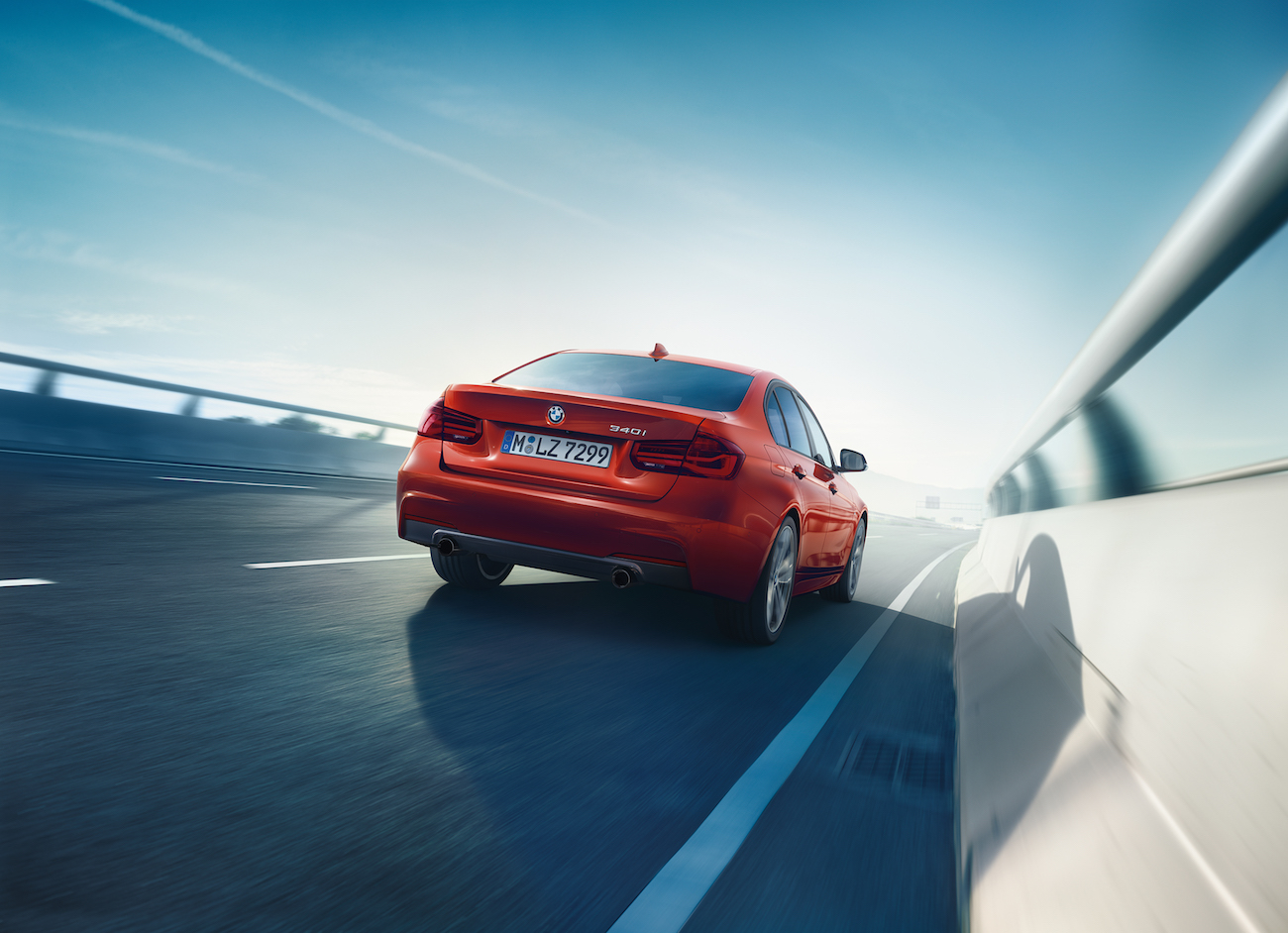 Roter BMW fährt auf einer Autobahn bei blauem Himmel und Sonnenschein, Seitenansicht von einem anderen Auto im Vordergrund.