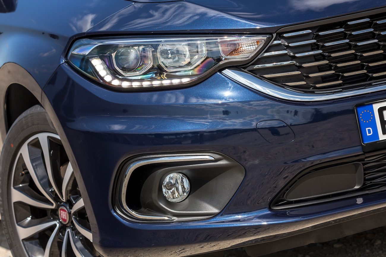 Nahaufnahme eines blauen Autos mit Fokus auf Scheinwerfer und Kühlergrill, darunter Nebelscheinwerfer und ein kleines Markenlogo.