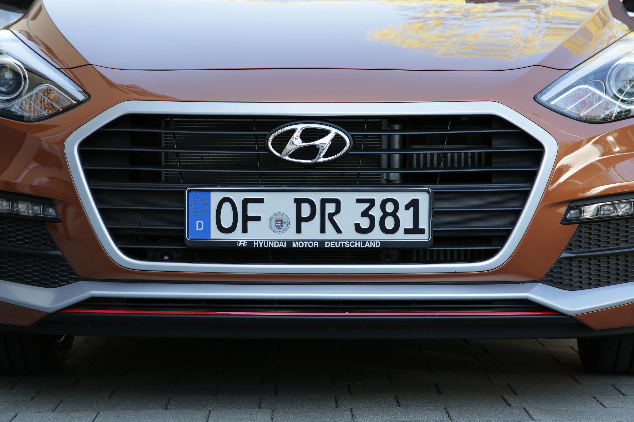 Brauner Hyundai mit deutschem Kennzeichen „OF PR 381“ auf einem gepflasterten Parkplatz, Ansicht von vorne.