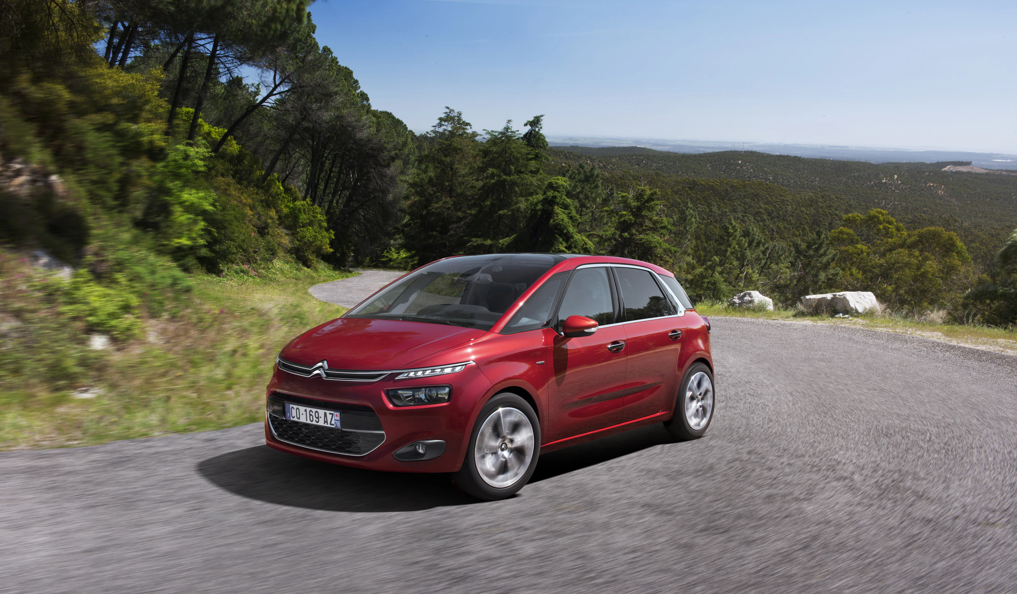 Roter Citroën C4 auf kurvenreicher Landstraße, umgeben von Wald und Hügellandschaft, bei sonnigem Wetter.