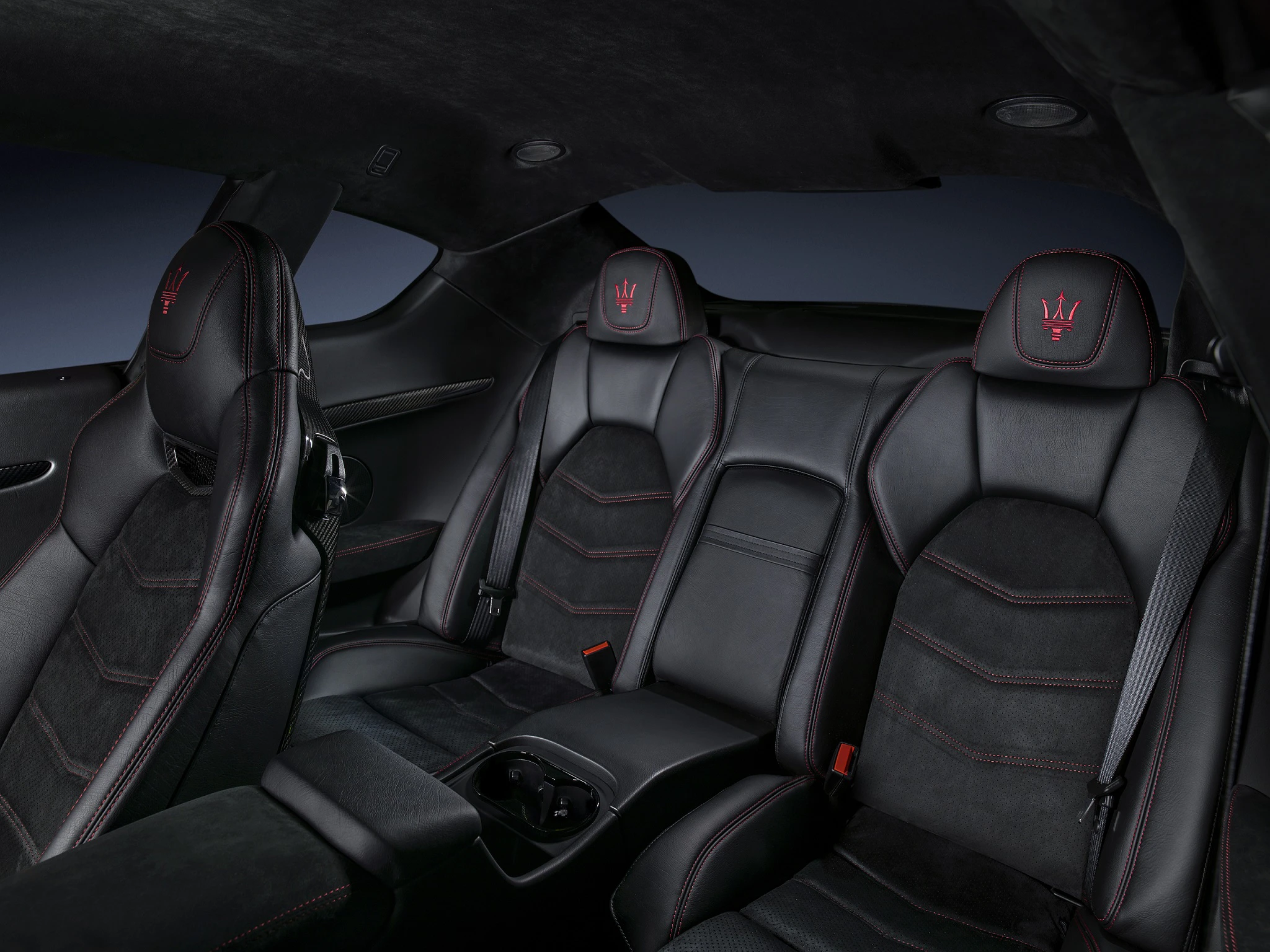 Innenraum eines luxuriösen Autos mit schwarzen Ledersitzen, roten Nähten und eingesticktem Logo auf den Kopfstützen. Rücksitze mit Mittelkonsole.