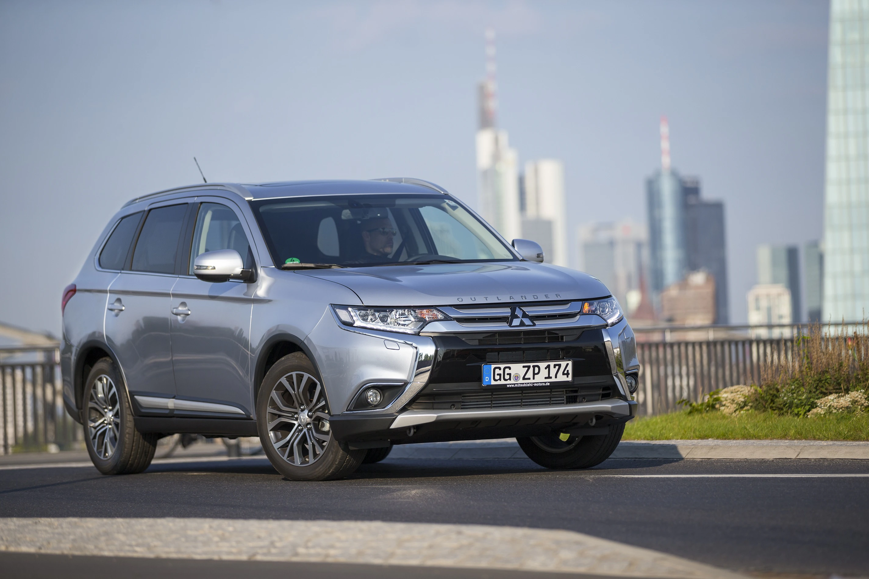 Silberner Mitsubishi SUV parkt auf einer Straße mit der Skyline einer Stadt im Hintergrund.