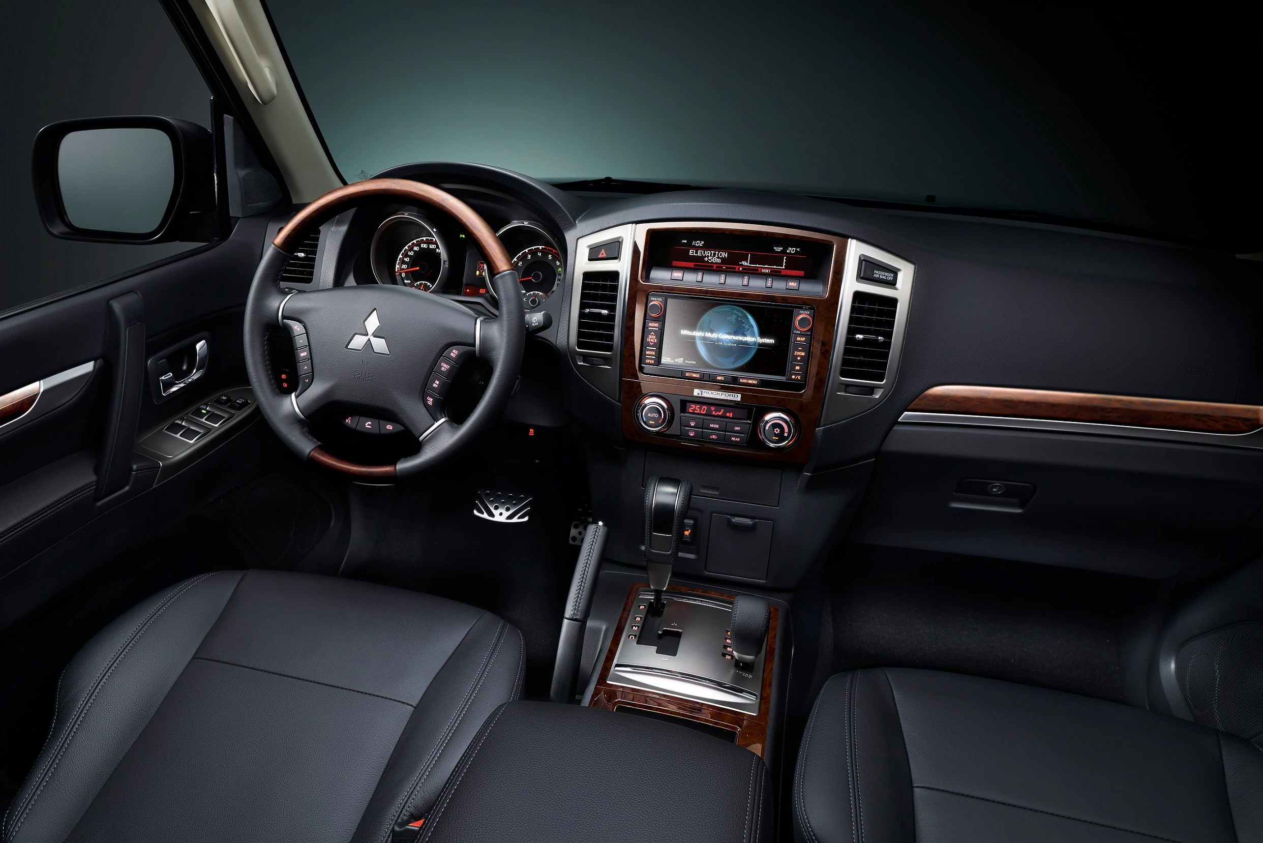 Innenansicht eines Autos mit dunklem Ledersitzen, Holzdekoren, Lenkrad mit Markenlogo, zentralem Touchscreen und Automatikgetriebe.