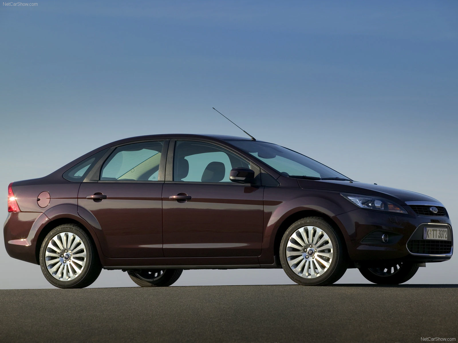 Dunkelroter Ford Focus Limousine auf einer Straße, seitliche Ansicht vor klarem Himmel.