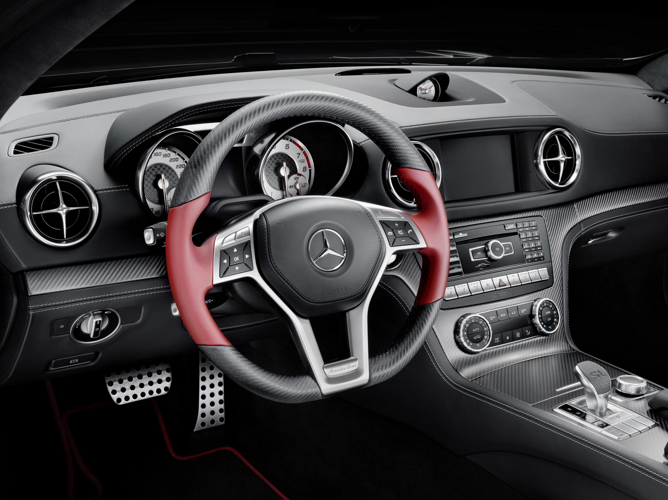 Nahaufnahme eines Mercedes-Innenraums mit einem markanten rot-schwarzen Lenkrad, modernen Armaturenbrettanzeigen und Bedienelementen.