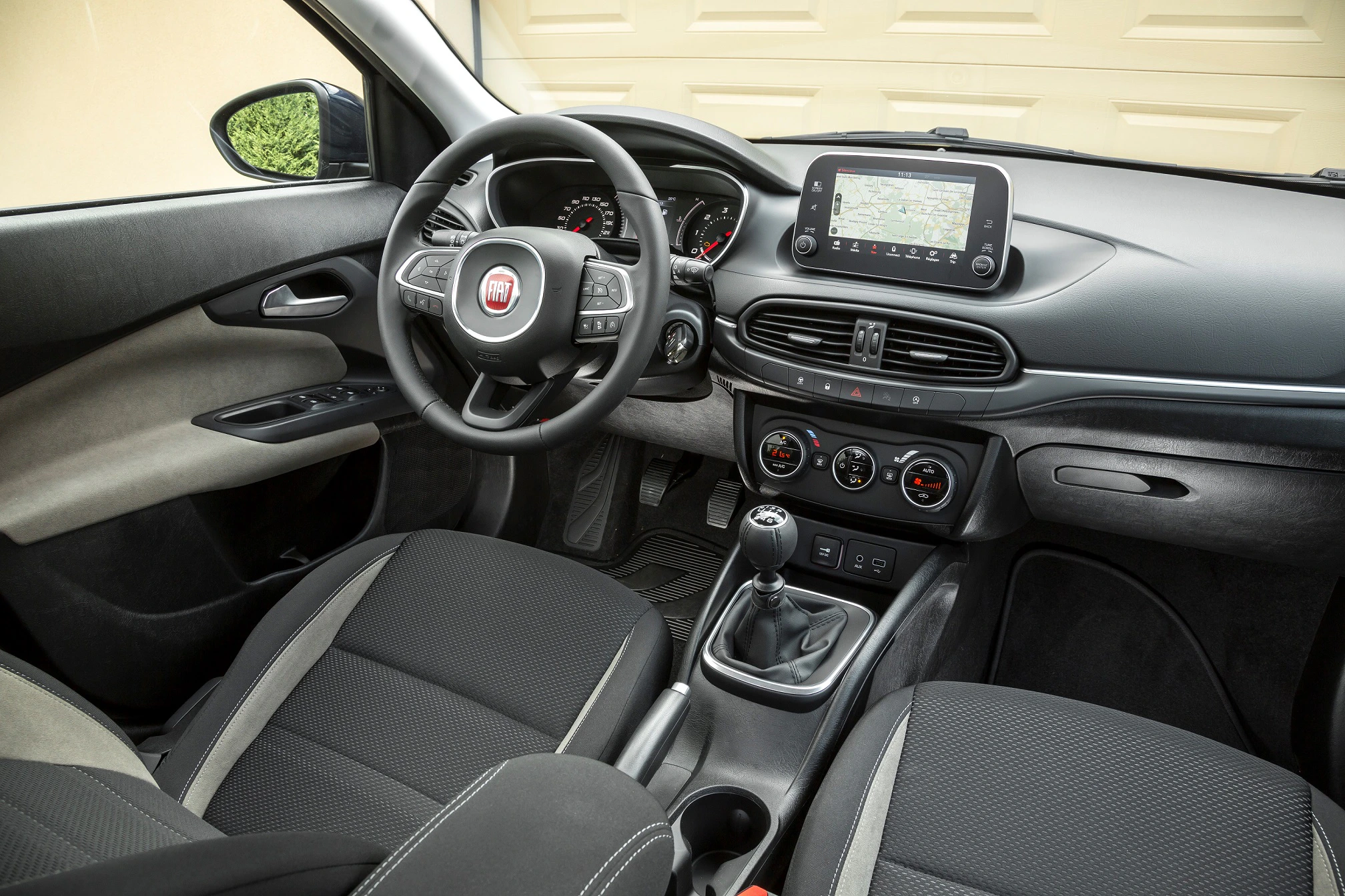 Innenraum eines Fiat-Autos mit schwarzem Armaturenbrett, Lenkrad, manuellem Schalthebel und Touchscreen-Navigationssystem.
