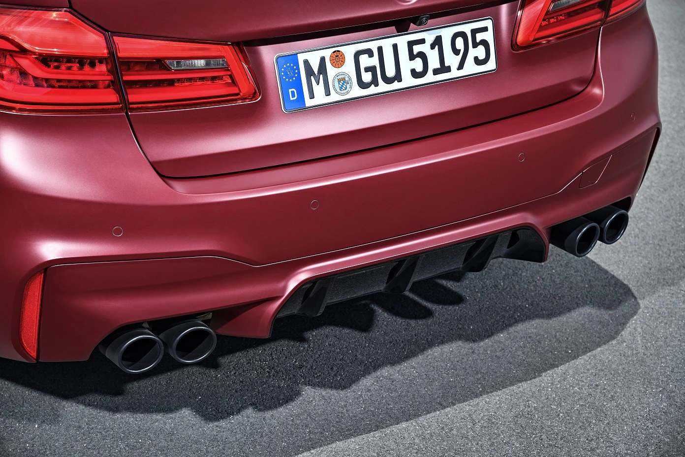 Rotes Auto-Heck mit Doppelauspuff, deutscher Kennzeichen "M GU 5195", Sportdesign, auf Asphaltstraße.