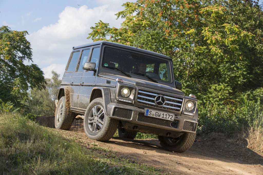 Ein silberner Mercedes-Geländewagen fährt abseits der Straße auf einem unbefestigten Weg durch eine grüne, bewaldete Landschaft.