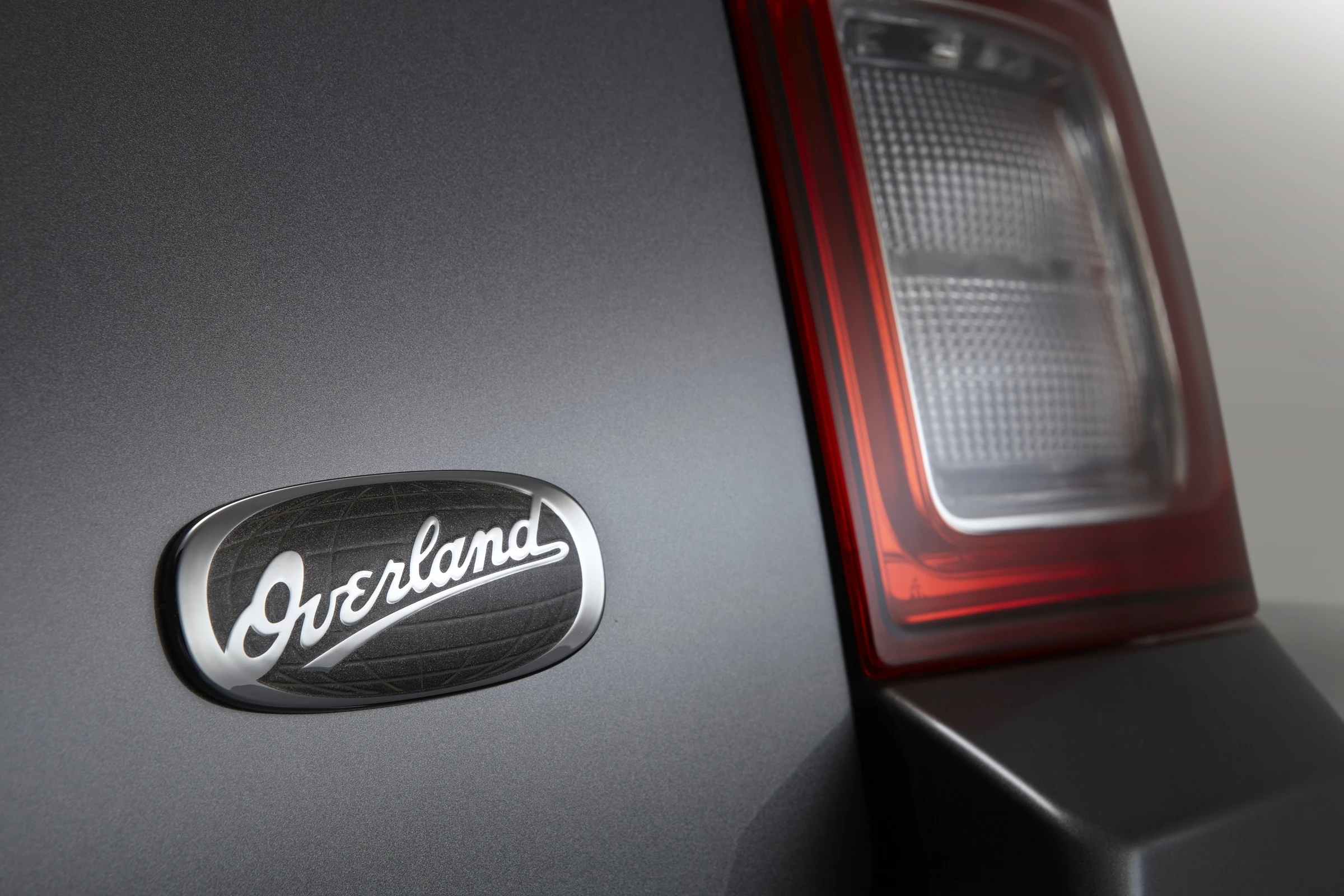 Nahaufnahme des Elegance-Schriftzugs "Overland" auf der Rückseite eines Autos, neben einer stilvollen Rückleuchte.