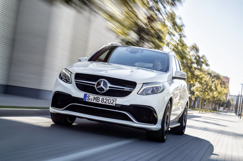 Weißer Mercedes-Benz SUV fährt auf einer städtischen Straße, umgeben von unscharfer Baumkulisse.