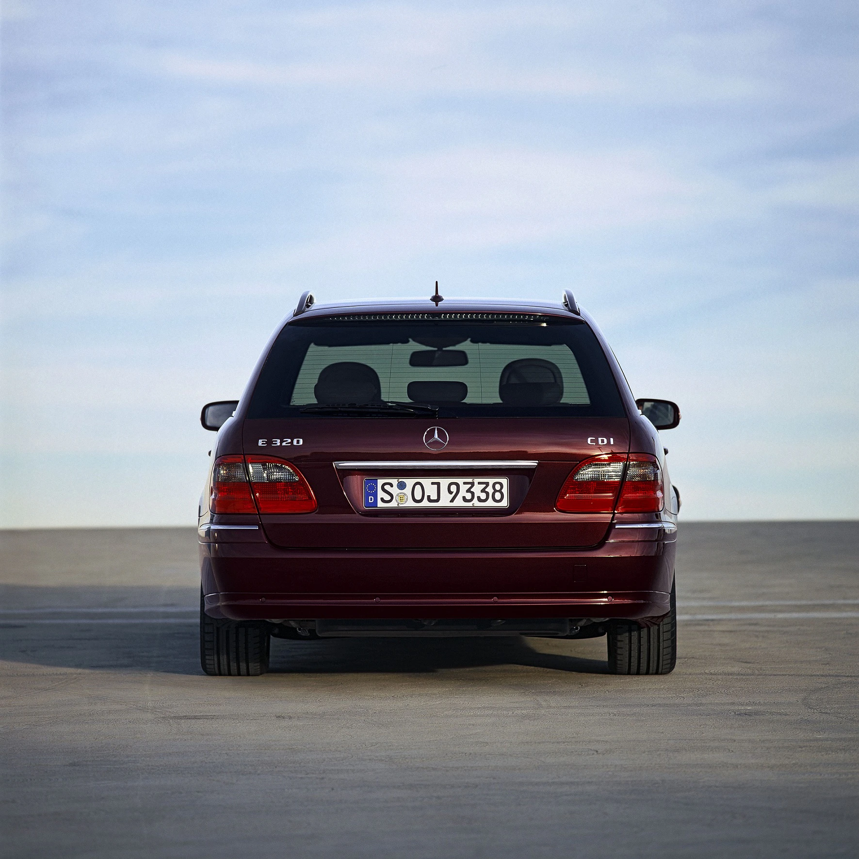 Roter Mercedes E 320 CDI Kombi von hinten auf einem Parkplatz, blauer Himmel im Hintergrund.