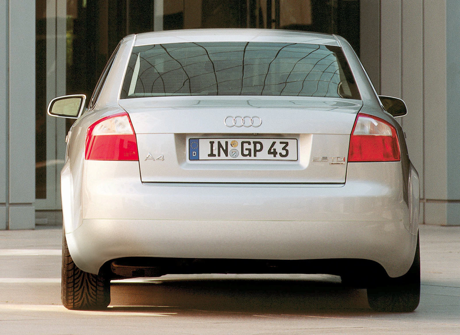 Rückansicht eines silbernen Audi A4 mit deutscher Kennzeichennummer „IN GP 43“, geparkt vor einem modernen Gebäude.