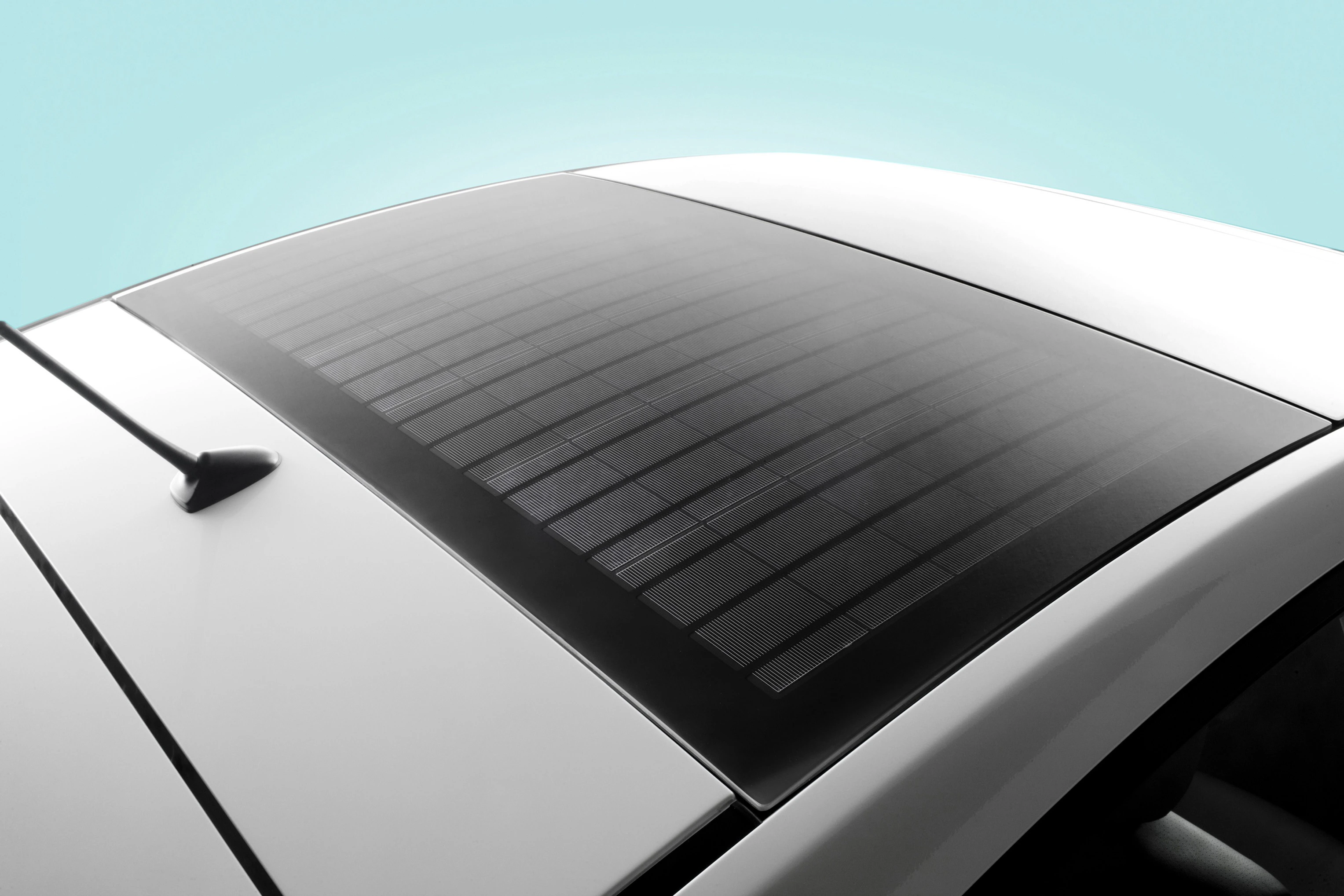 Ein Auto mit solarbetriebenem Dach auf hellblauem Hintergrund. Sicht auf das glatte Solarpanel in der Mitte der Dachfläche.