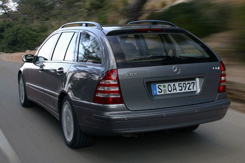 Silberner Mercedes-Benz C 200 Kombi fährt auf einer Landstraße, umgeben von Bäumen. Fahrzeug ist von hinten zu sehen.