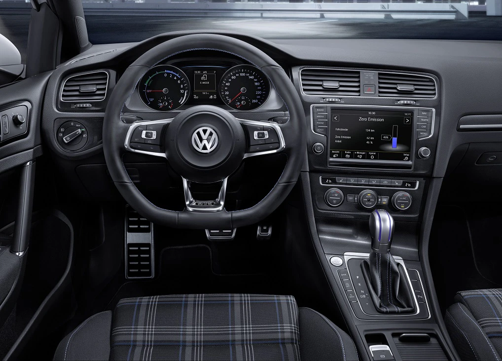 Innenraum eines VW-Autos mit Lenkrad, Tachometer, Display und Schalthebel. Die Sitze haben ein karierte Muster.