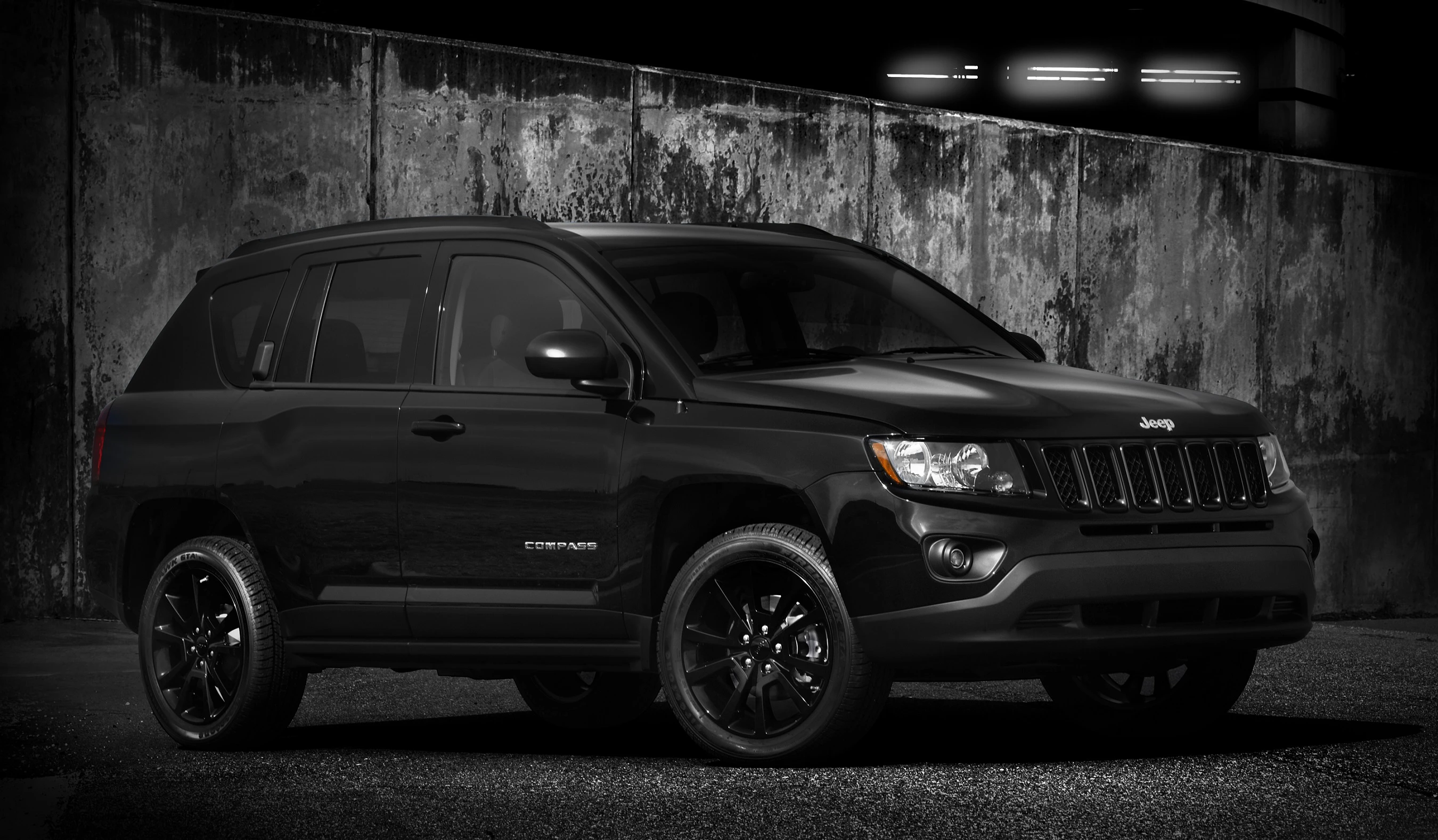 Schwarzer Jeep Compass vor einer Betonwand bei Nacht, stilvoll beleuchtet und in einem ruhigen, urbanen Setting dargestellt.