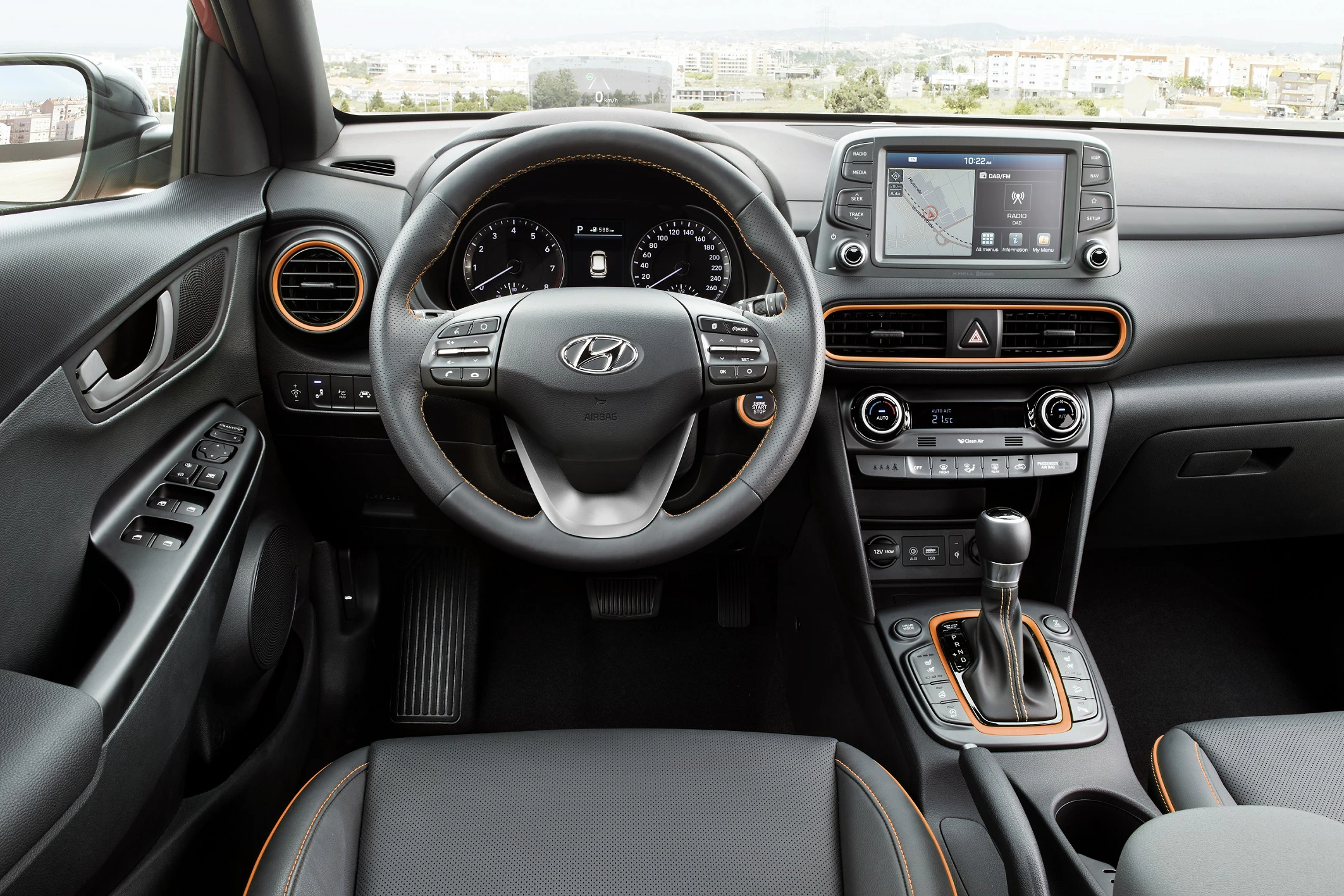 Innenraum eines Hyundai-Autos mit Lenkrad, Tachometer, Multimedia-Bildschirm und Schalthebel. Moderne Gestaltung mit Akzenten in Orange.
