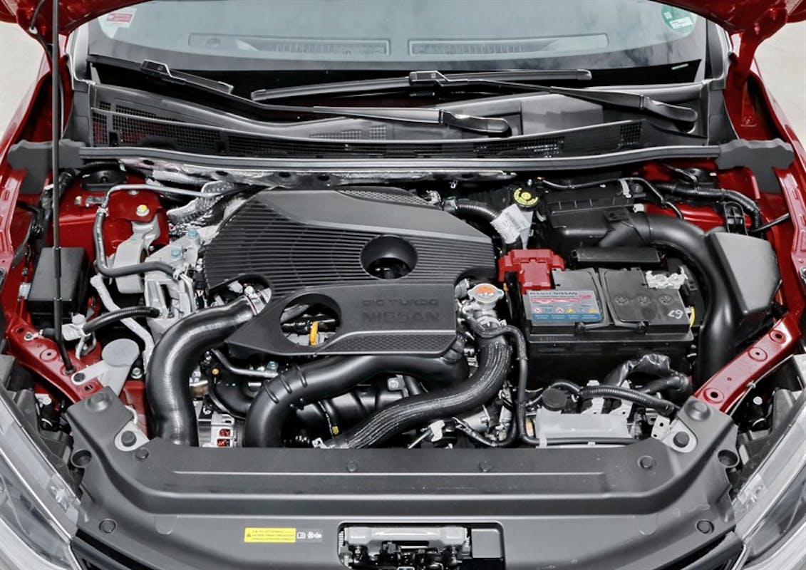 Motorraum eines roten Autos, der einen modernen Verbrennungsmotor mit mehreren Schläuchen, Kabeln und Batterien zeigt.