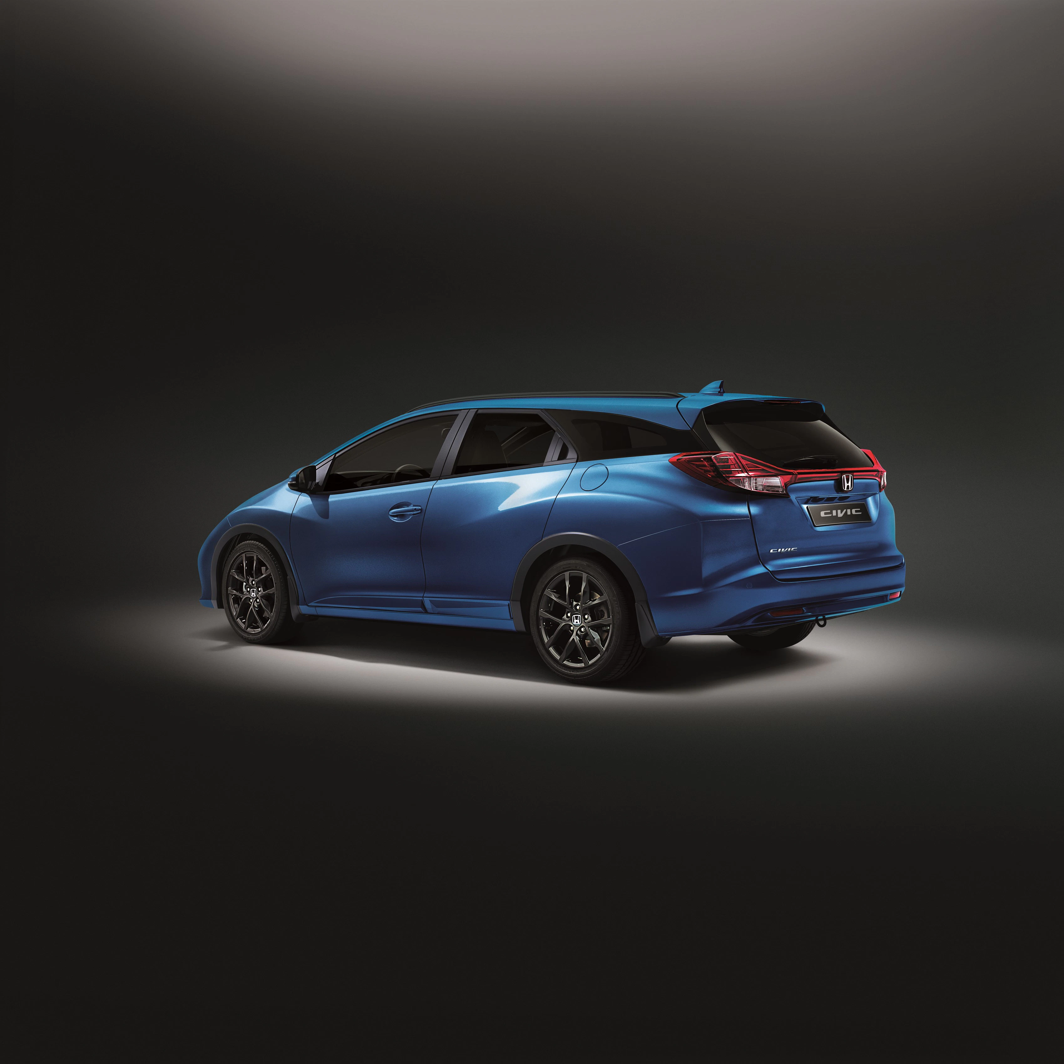 Blauer Honda Civic Kombi in einem Studio mit Beleuchtung von oben, Sicht von hinten links, dunkler Hintergrund.