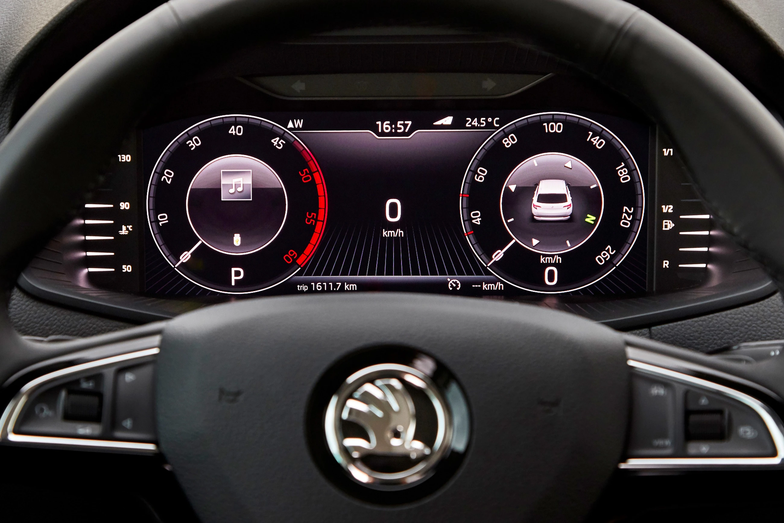 Digitales Armaturenbrett eines Autos mit Tachometer, Drehzahlmesser und Musik-Icon, Lenkrad mit Markenlogo im Vordergrund.