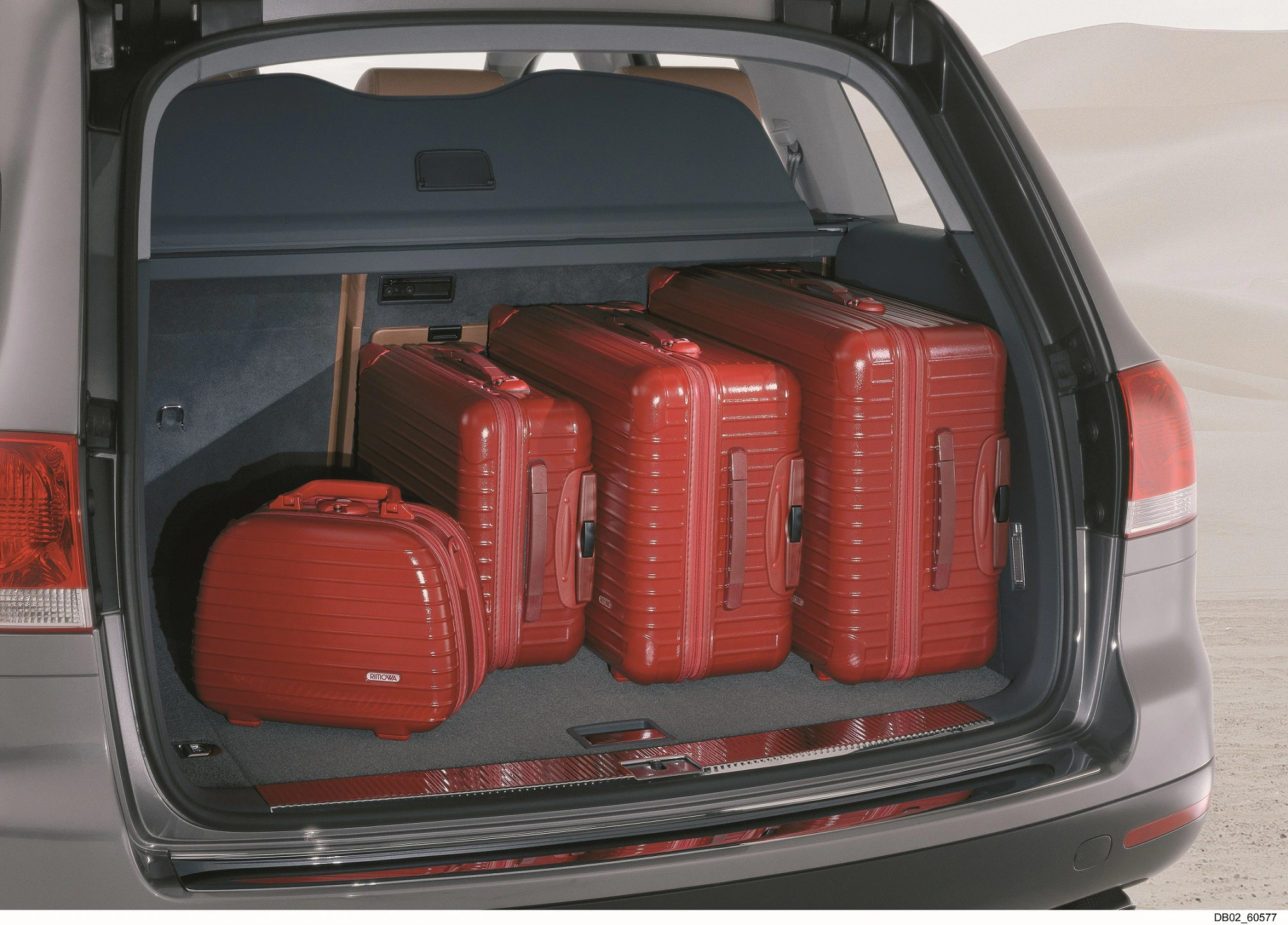 Drei große und ein kleines rotes Hartschalenkoffer-Set im Kofferraum eines Autos, bereit für eine Reise.