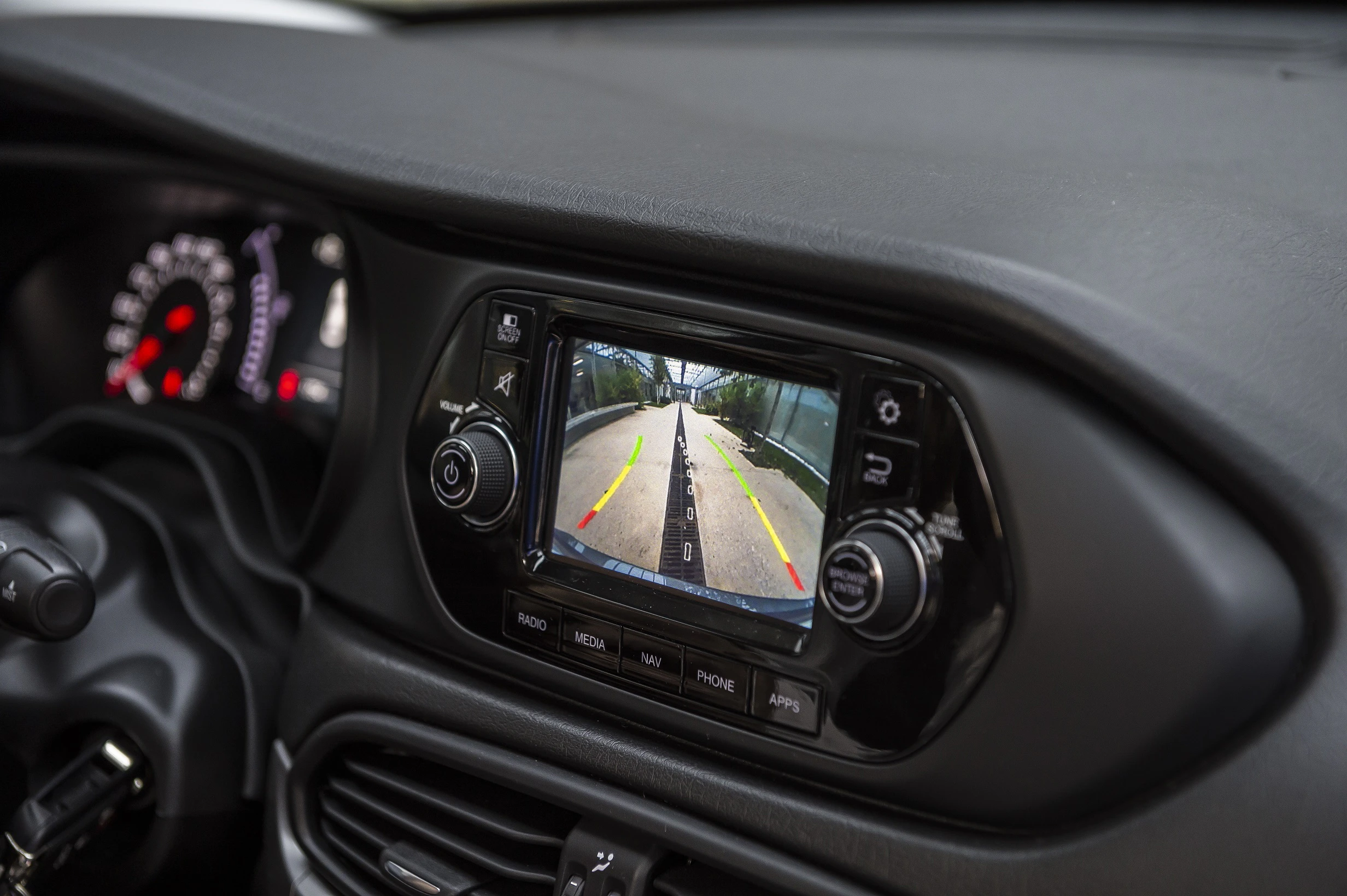 Display eines Autos mit Rückfahrkamera, zeigt Straße und Markierungen an. Umgeben von Tasten und Steuerungen im Armaturenbrett.