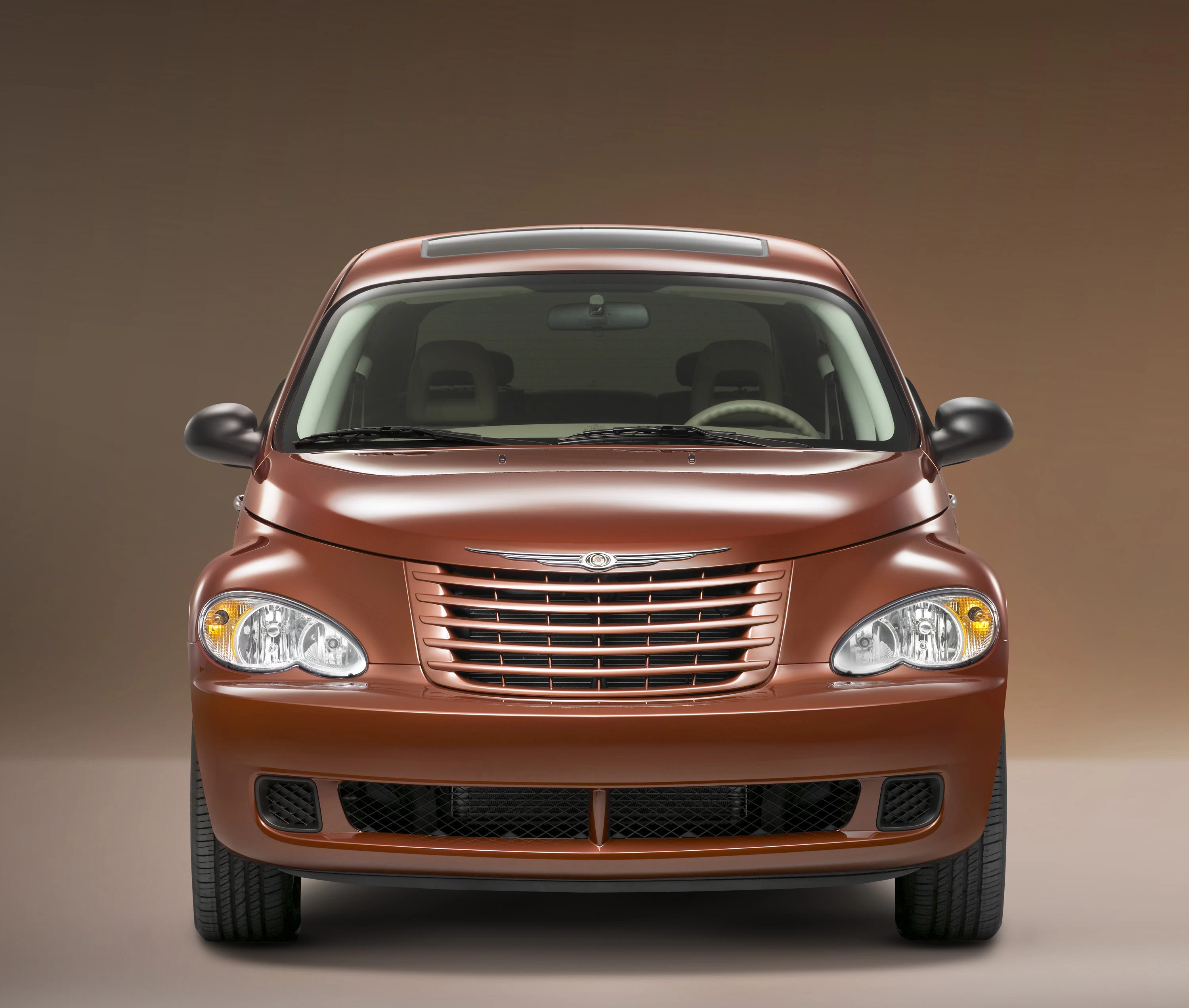 Brauner Chrysler PT Cruiser, Frontalansicht, mit charakteristischem Kühlergrill und abgerundeter Karosserie vor neutralem Hintergrund.