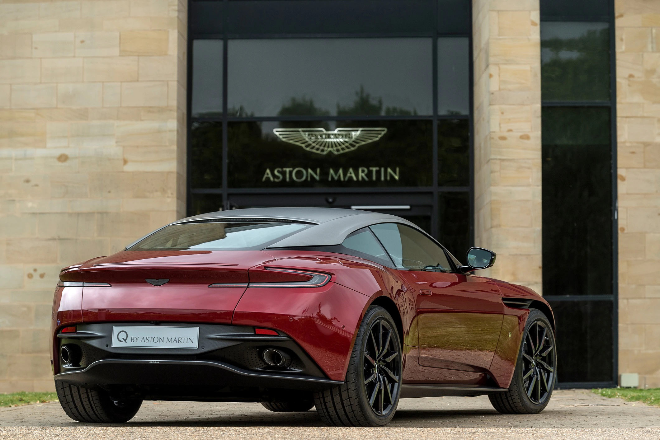 Roter Aston Martin Sportwagen vor einem Gebäude mit Aston Martin Logo, Rückansicht.