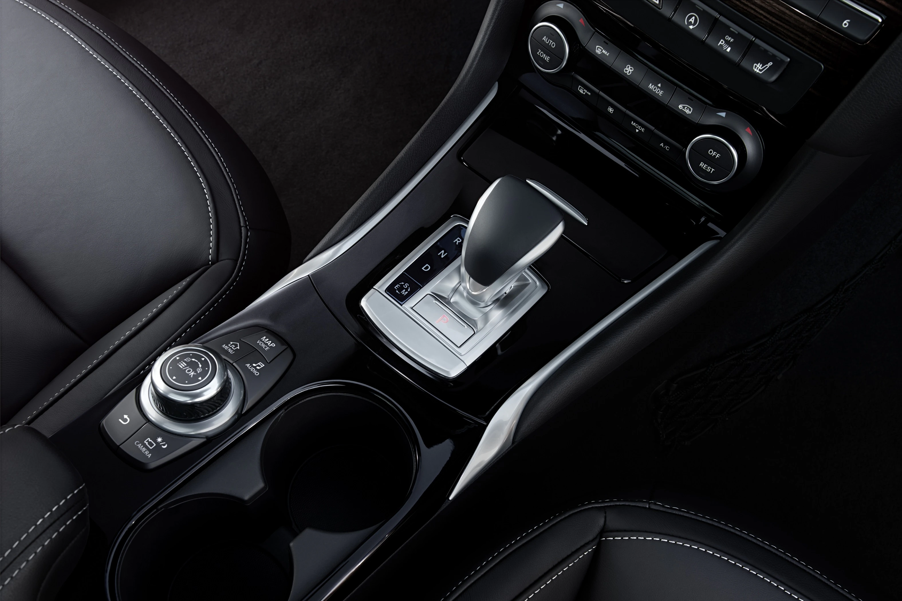Nahaufnahme einer modernen schwarzen Mittelkonsole in einem Auto mit Schalthebel, Drehregler und Getränkehaltern.