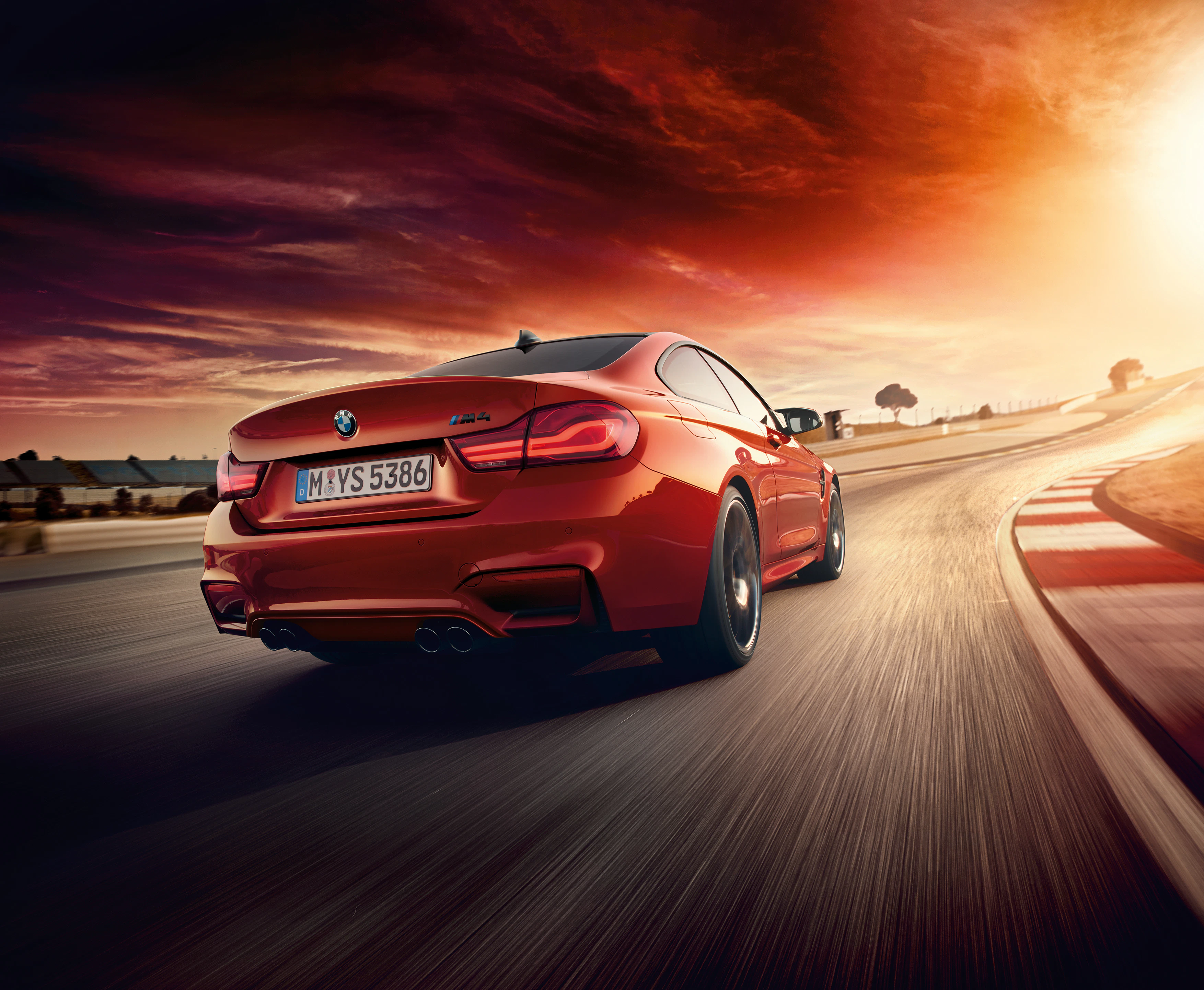 Roter BMW fährt bei Sonnenuntergang auf einer kurvigen Straße, dynamisch und sportlich in Szene gesetzt.