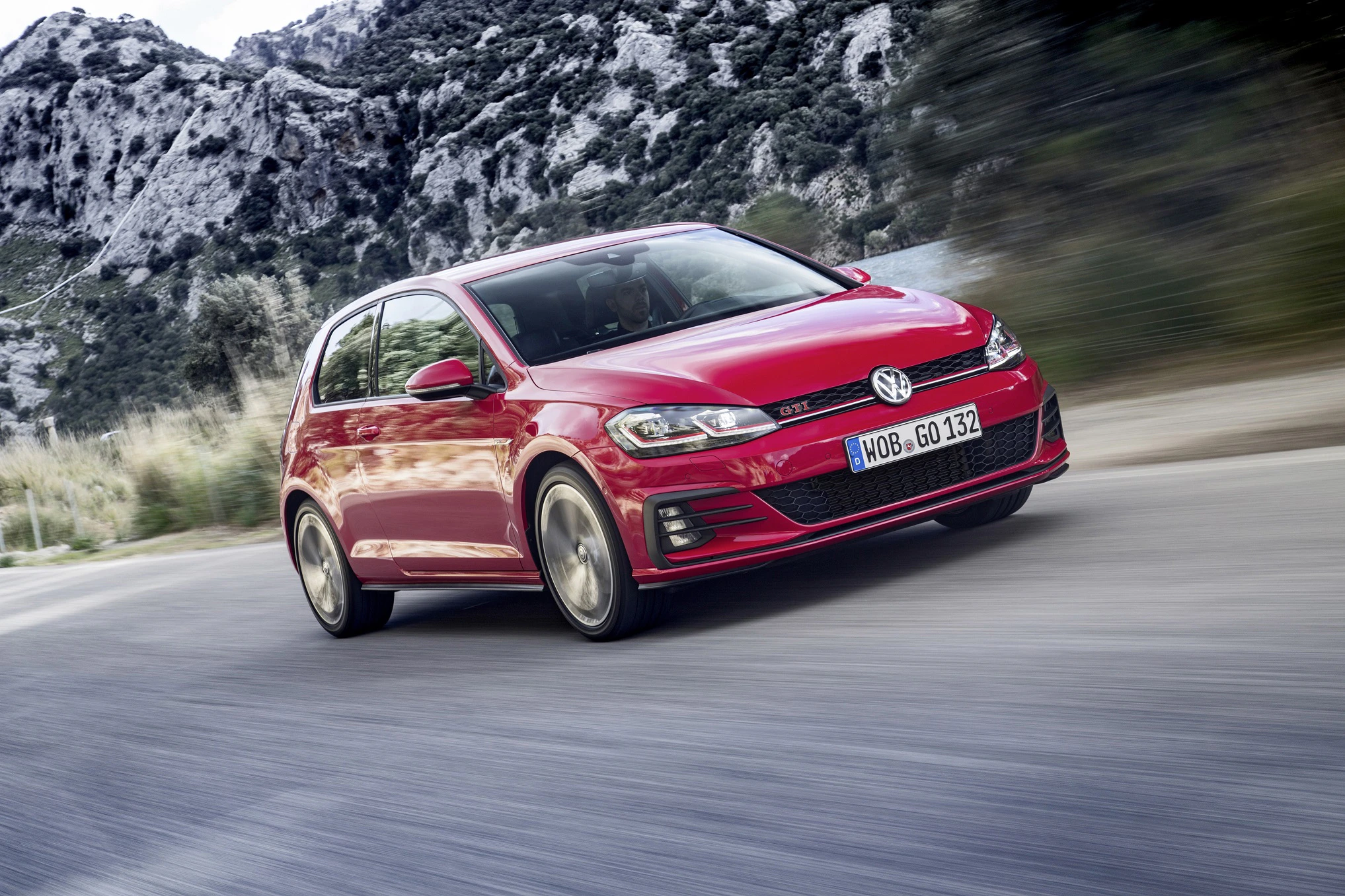 Roter VW Golf fährt dynamisch auf einer Straße mit beeindruckender Bergkulisse im Hintergrund.