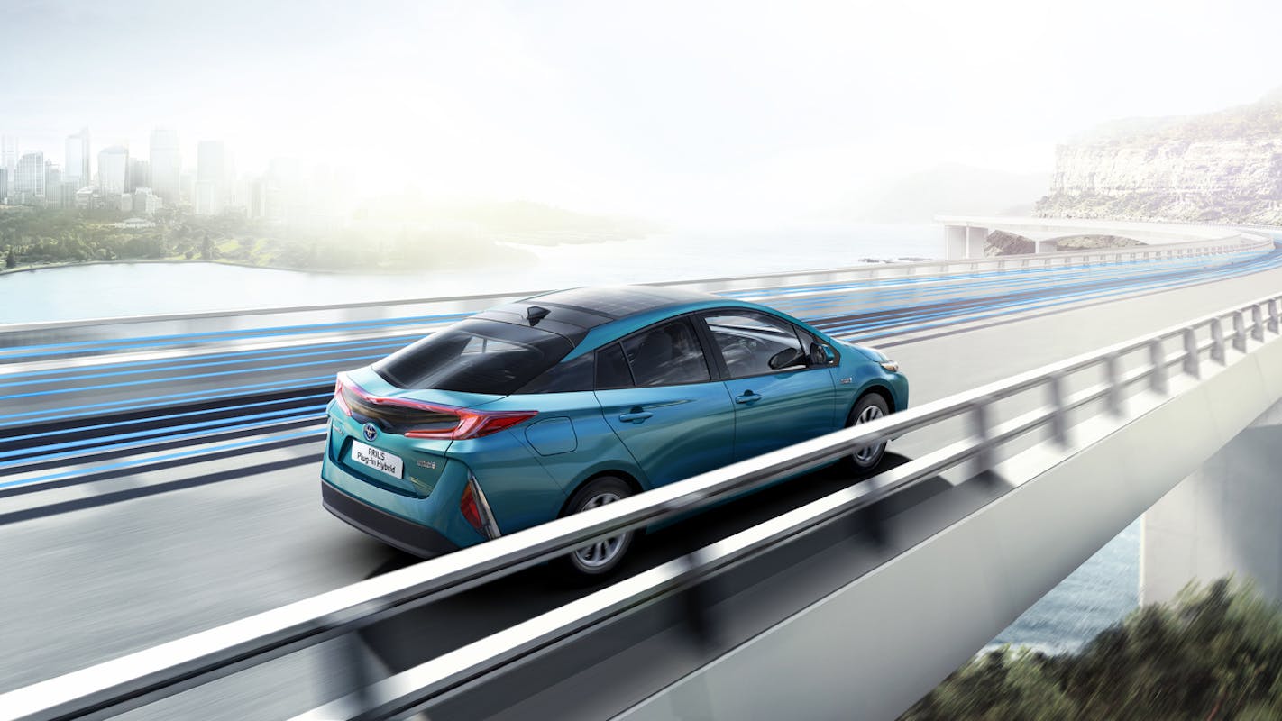 Blaues Auto fährt über eine futuristische Brücke mit Stadt- und Wasserlandschaft im Hintergrund, bei klarem Himmel.