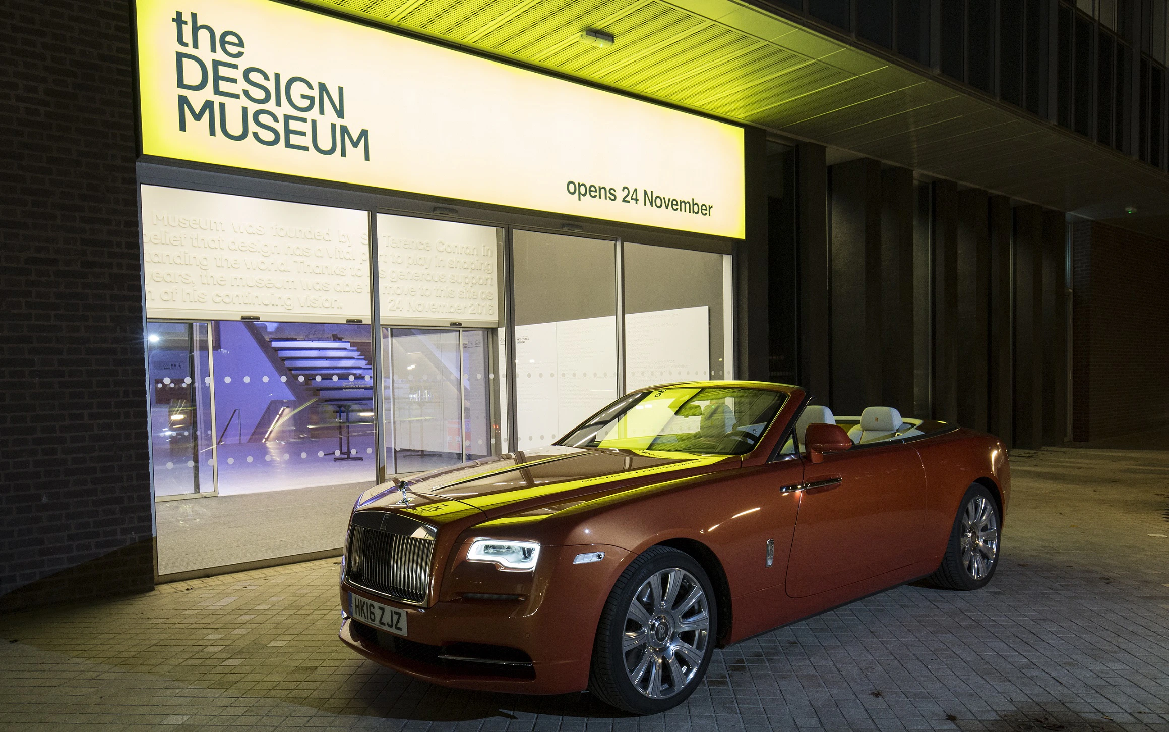 Luxus-Cabrio parkt nachts vor dem Design Museum. Gebäude mit heller Werbetafel und Glasfront. Eleganter, stilvoller Auftritt.