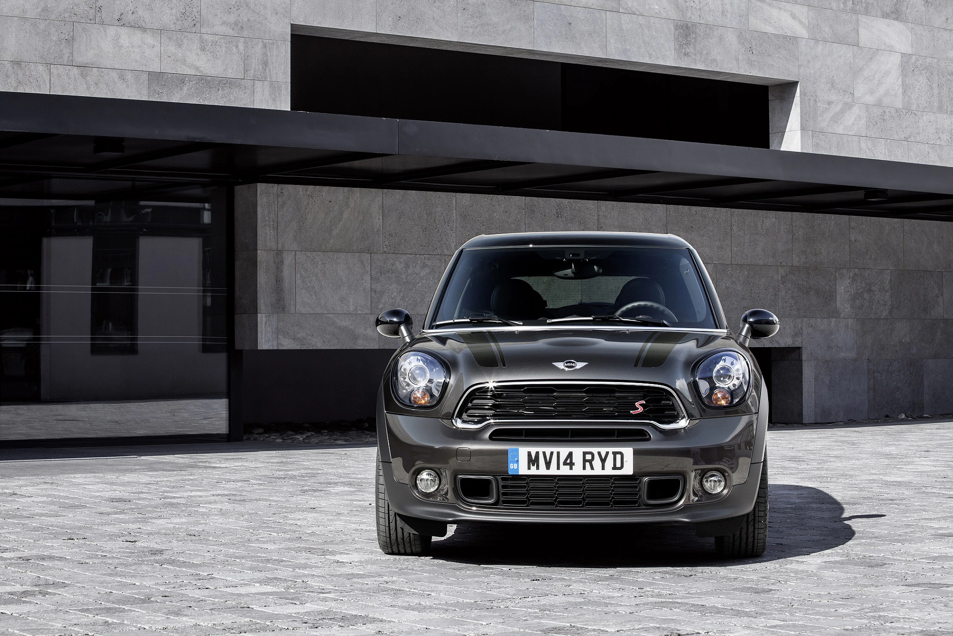Ein grauer Mini Cooper steht vor einem modernen Gebäude mit einer Steinfassade auf einem grauen Pflasterweg.
