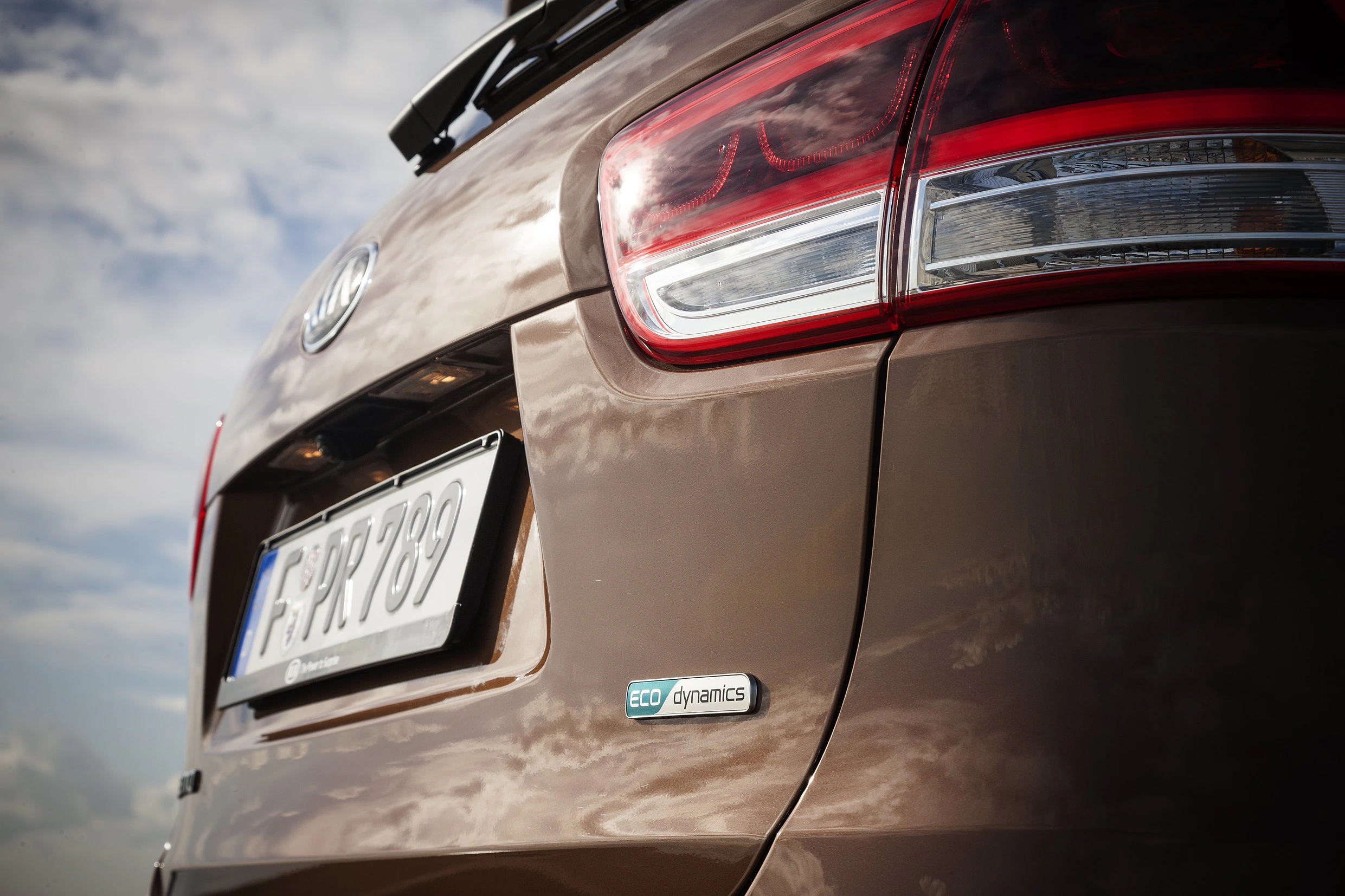 Nahaufnahme eines braunen Autos mit deutschem Kennzeichen, roten Rücklichtern und „ECO dynamics“-Emblem, vor bewölktem Himmel.