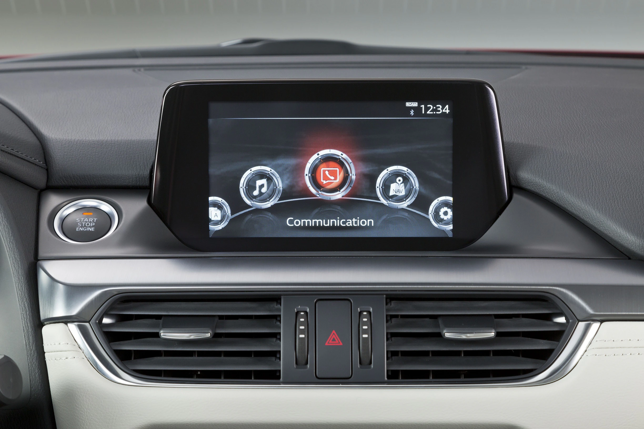 Autoinnenraum mit digitalem Display; zentrales Menü mit Kommunikationssymbolen; Lüftungsschlitze darunter; Startknopf links.