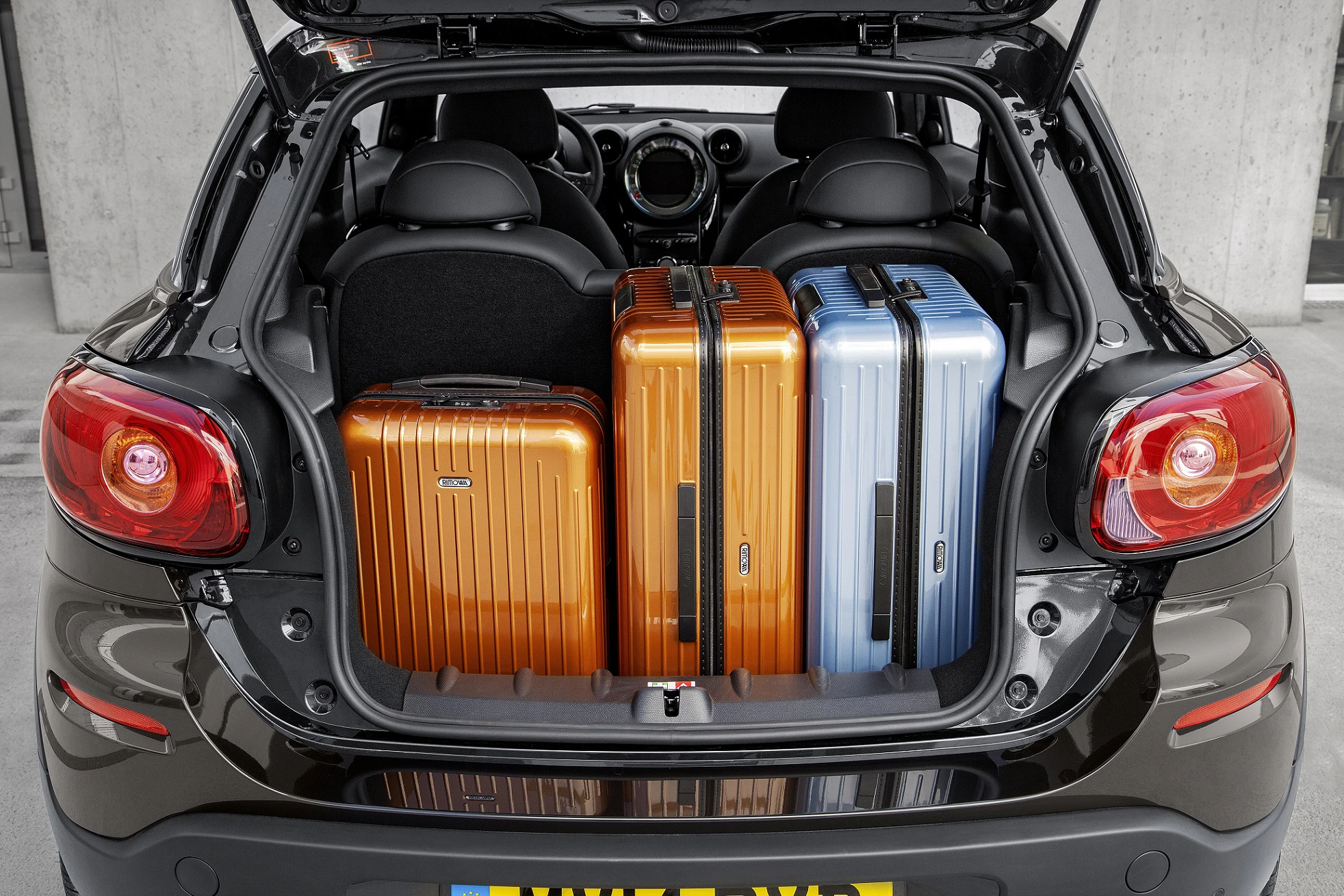 Kofferraum eines Autos mit drei Hartschalenkoffern: zwei orangefarbene und ein blauer, eng nebeneinander platziert.