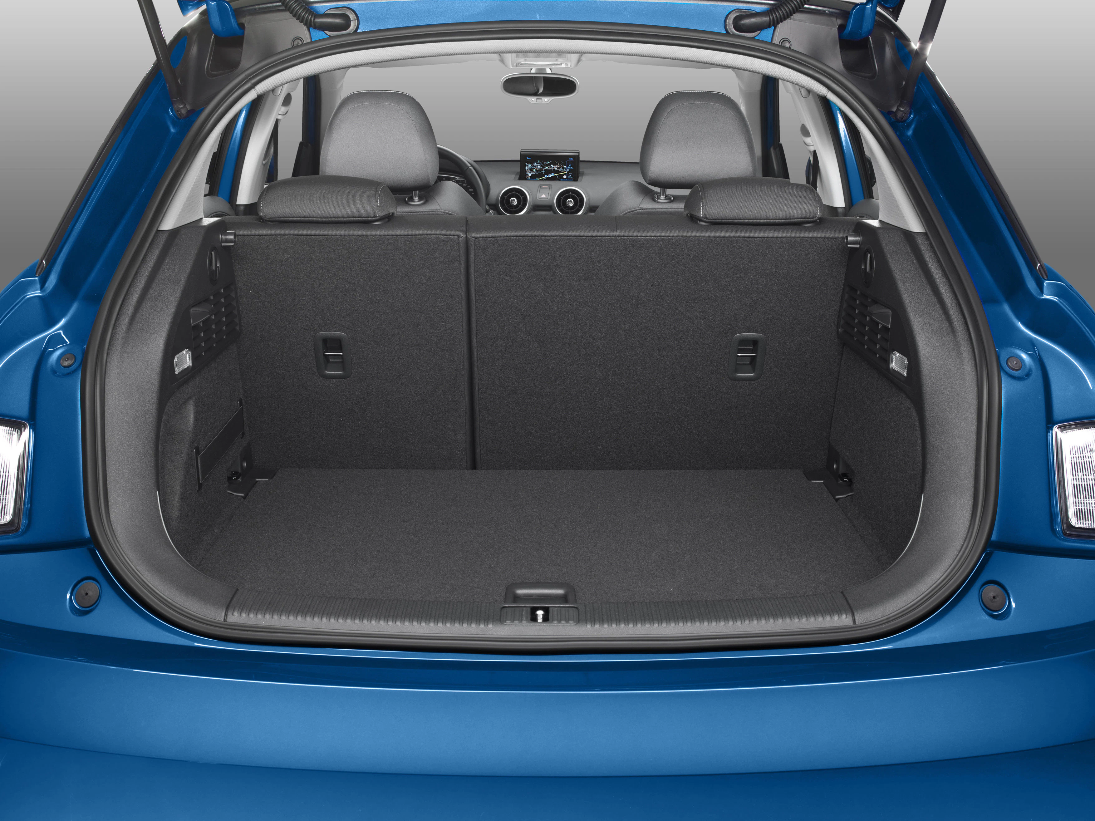Offener Kofferraum eines blauen Autos mit umgeklappten Rücksitzen, graue Innenausstattung sichtbar, Lenkrad im Hintergrund.
