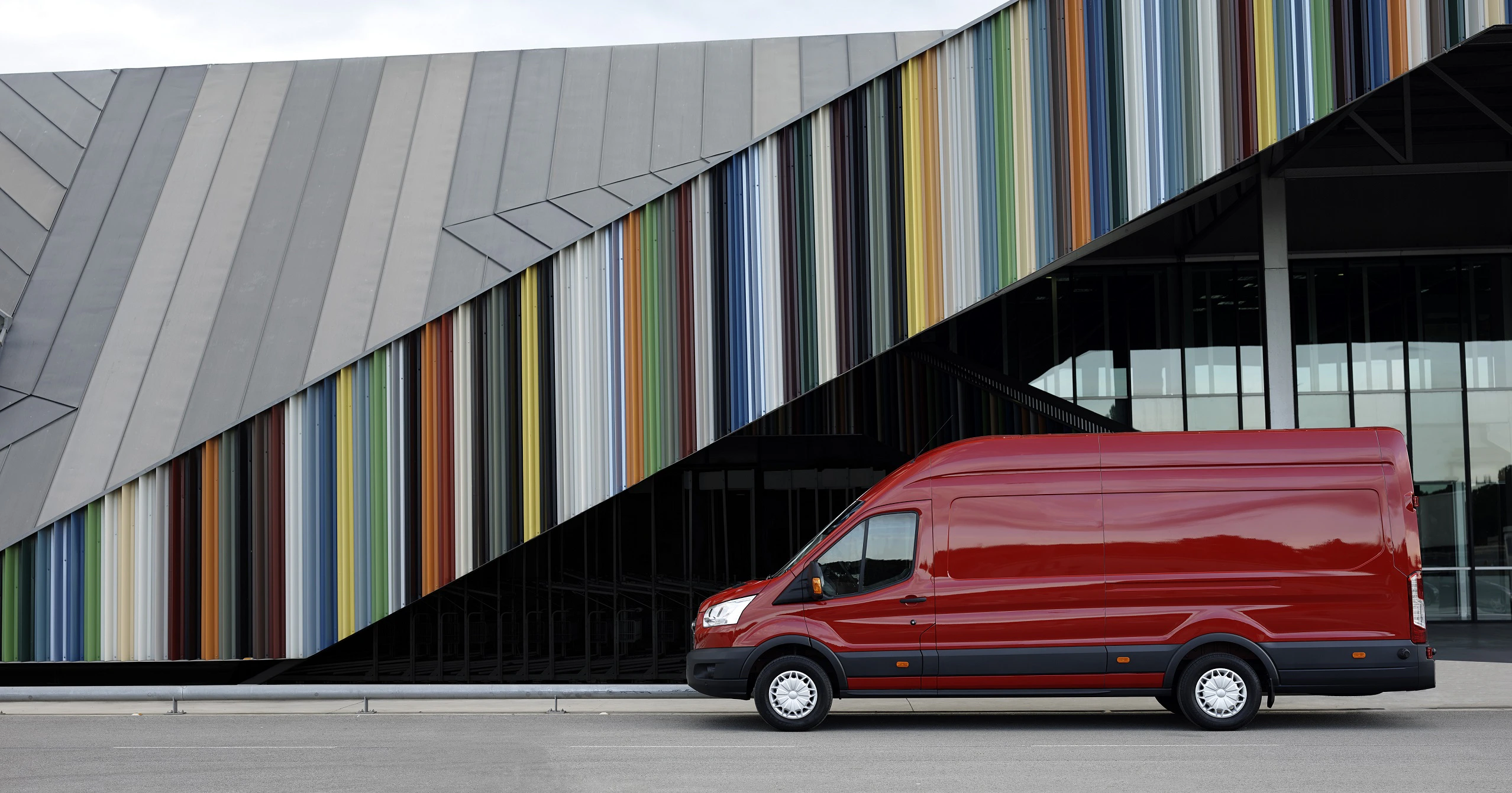 Roter Lieferwagen vor einem modernen Gebäude mit diagonalen, bunten Streifen.