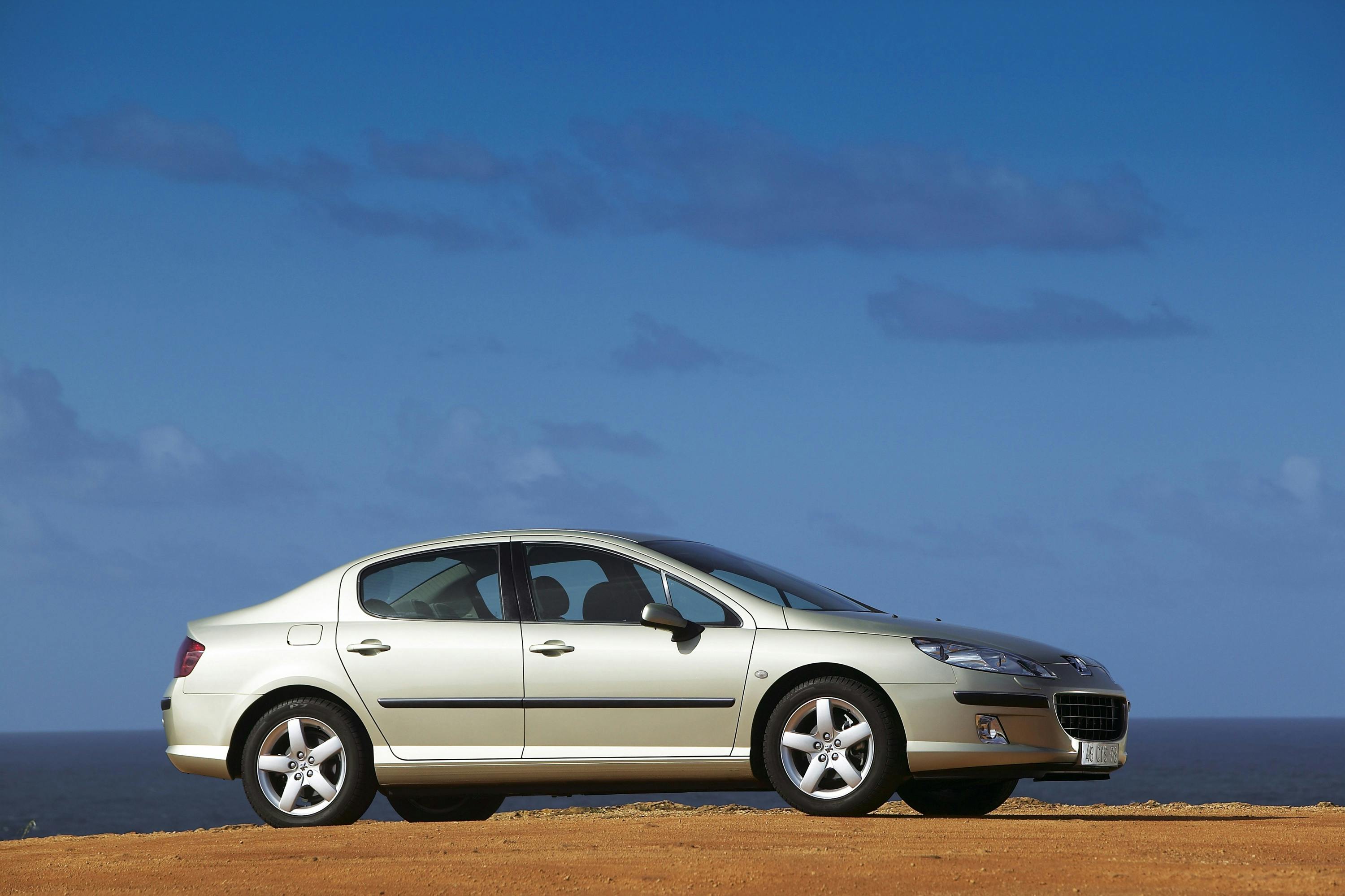 Silberner Pkw, seitlich fotografiert, steht auf einer sandigen Fläche vor blauem Himmel und Meereshorizont im Hintergrund.